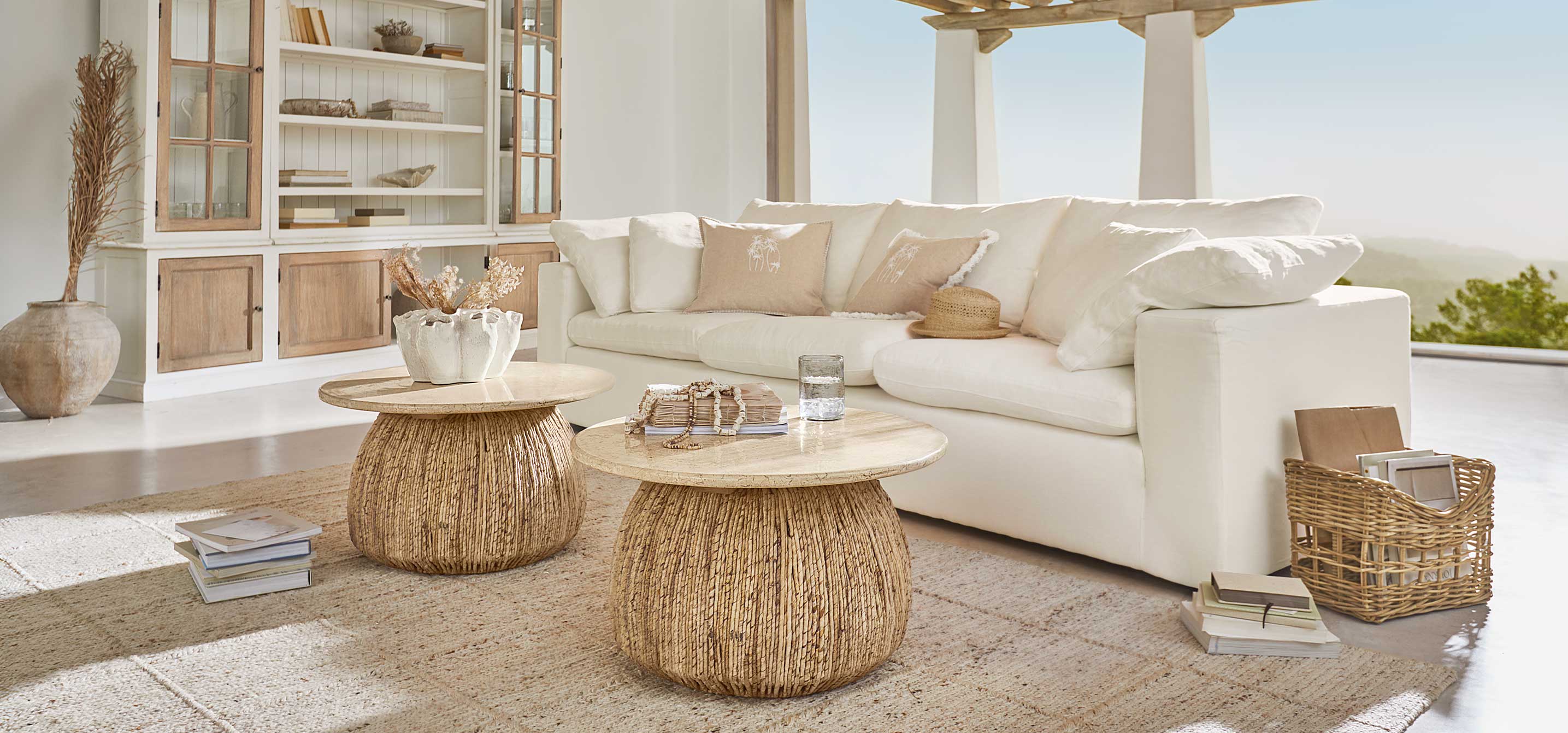 Twee ronde salontafels van natuurlijk hout en riet in lichte woonkamer met witte bank