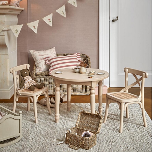 Ronde houten tafel met twee stoelen en een rieten mand op een vloerkleed in lichte kinderkamer