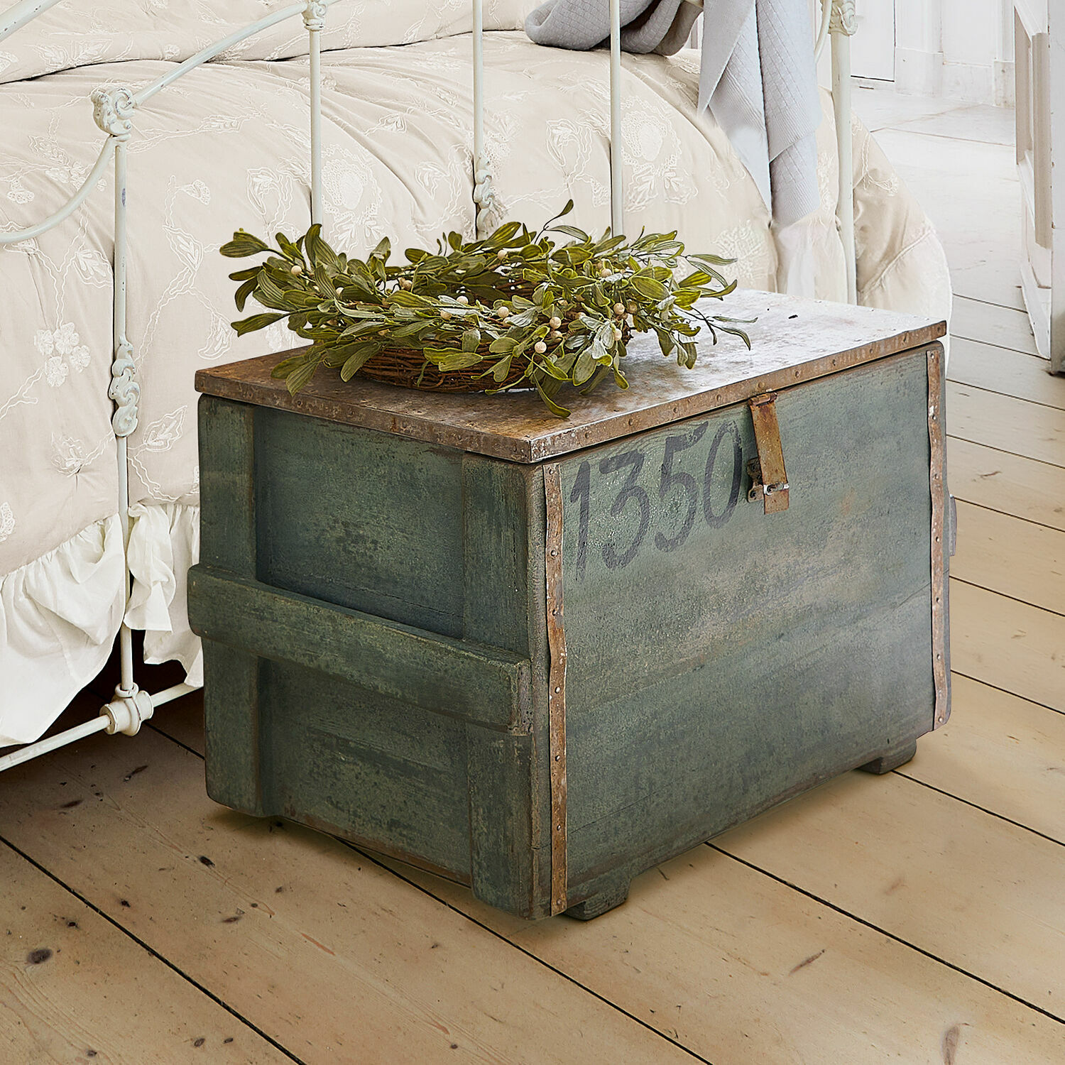 Groene metalen kist met nummer 1350 en groene bladdecoratie op lichte houten vloer