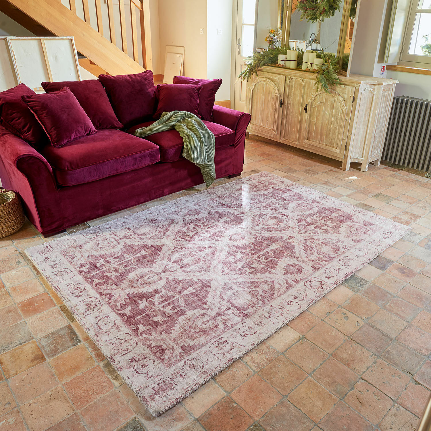 Roze vintage vloerkleed met patroon voor bordeauxrode fluwelen bank en lichte houten kast