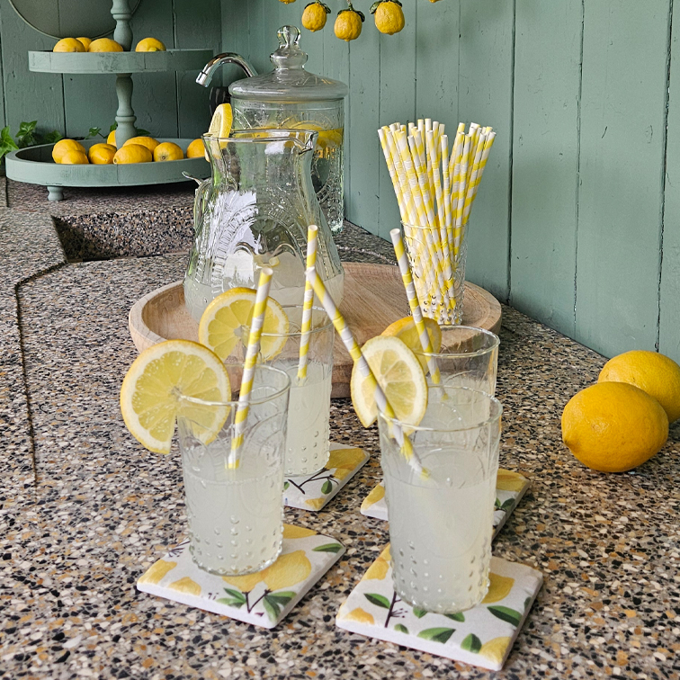 Glazen limonade met citroenschijfjes op stenen aanrecht met papieren rietjes en dienblad met citroenen