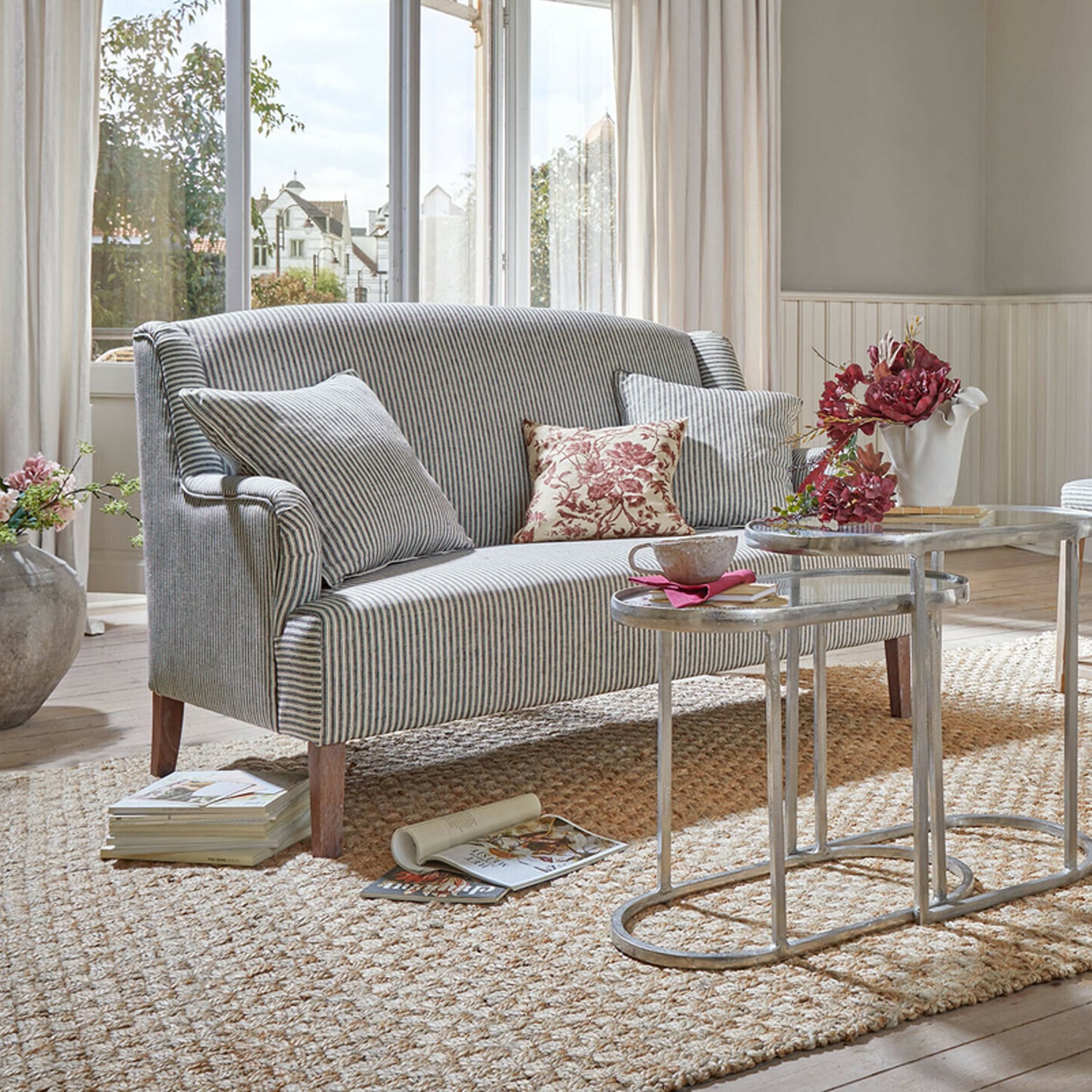Gestreepte stoffen bank in grijs-witte tinten met kussens en metalen salontafels in lichte woonkamer