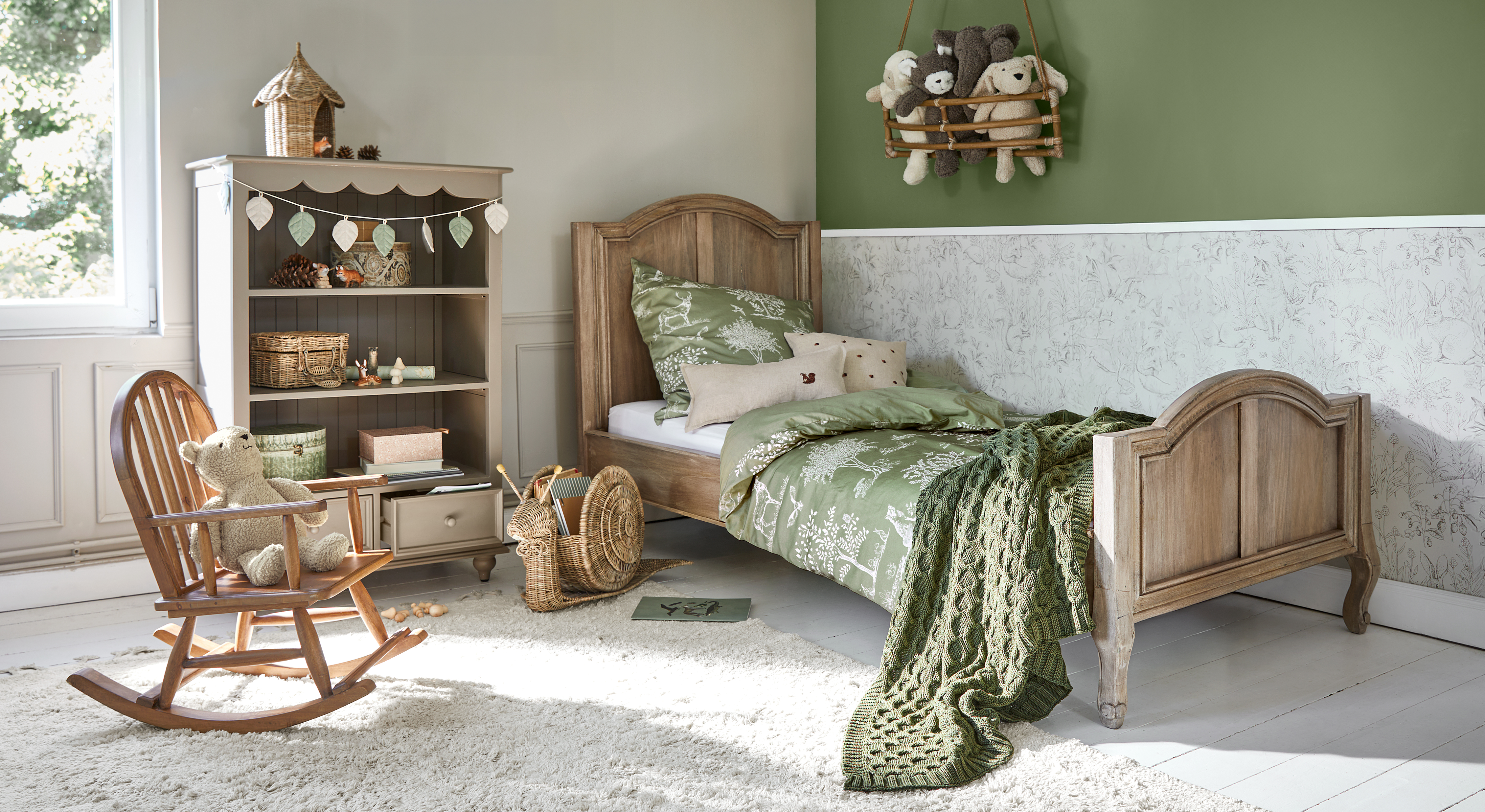Houten kinderbed met groene beddengoed en deken, gezellige kamer met schommelstoel en knuffelbeer