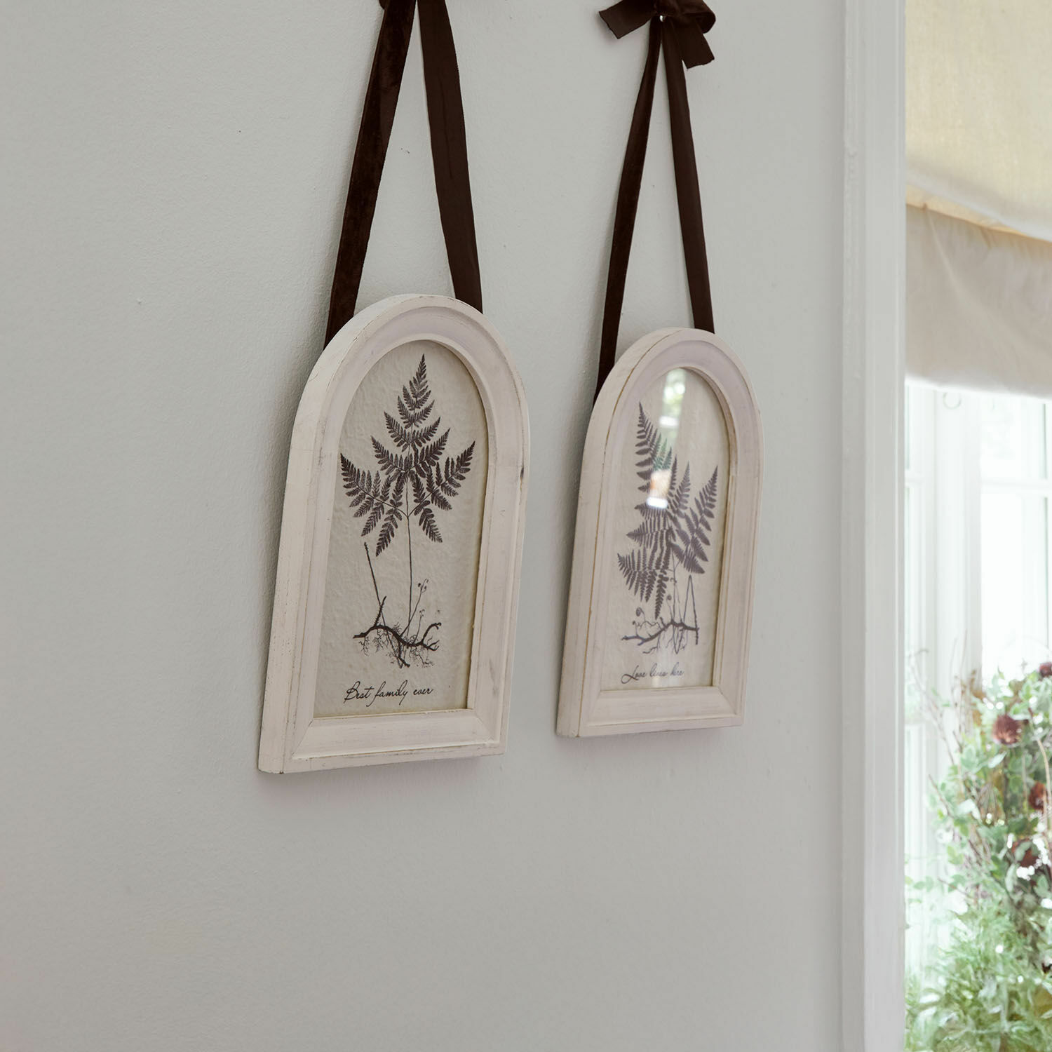 Twee witte houten lijsten met varenafbeeldingen en bruine linten om aan de muur te hangen