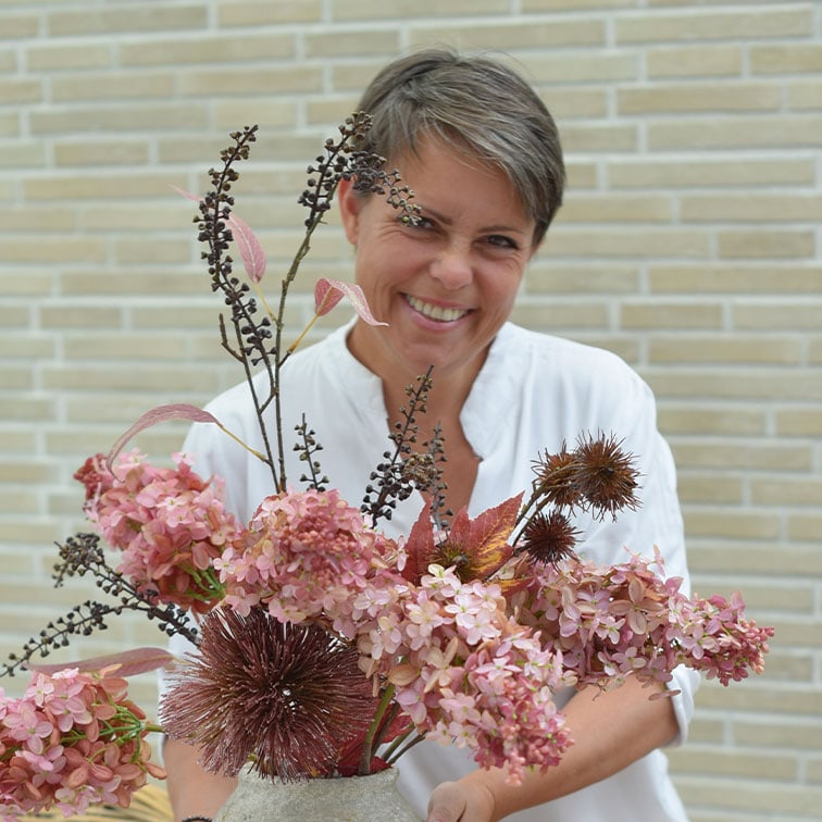 Vrouw in wit overhemd houdt vaas met roze en bruine gedroogde decoratieve bloemen vast