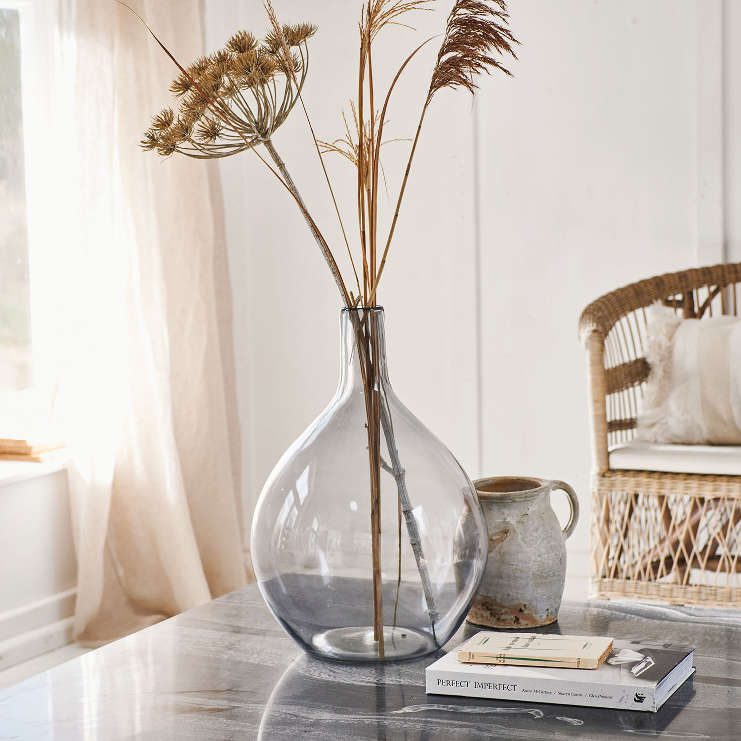 Transparante glazen vaas met gedroogde grassen op marmeren tafel in lichte kamer