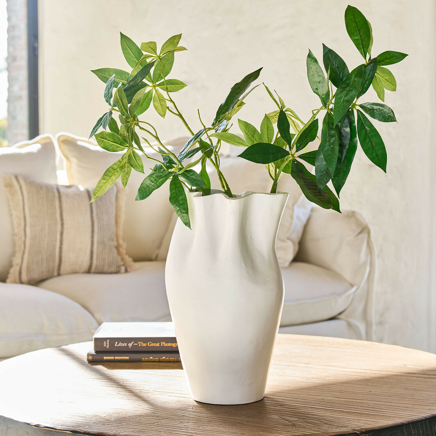 Witte keramische vaas met golvende vorm en groene bladeren op houten tafel in woonkamer