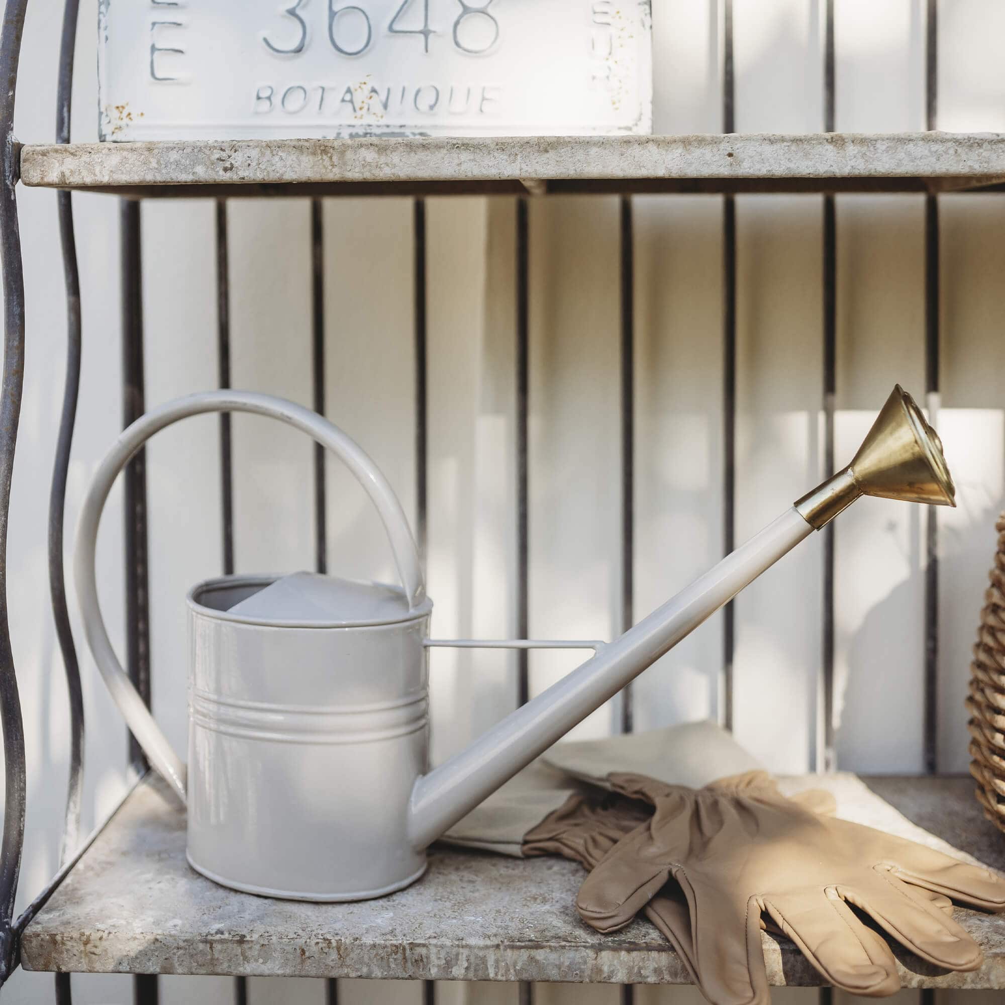 Beige metalen gieter met messing sproeikop en tuinhandschoenen op stenen plank