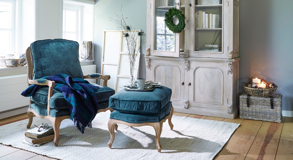 Fluwelen blauwe stoel met houten frame en voetenbank in gezellige woonkamer met decoratie