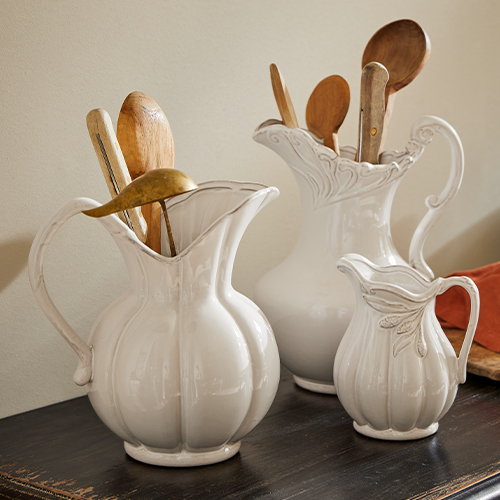 Set van drie witte keramische kannen met decoratief patroon, gevuld met houten keukengereedschap