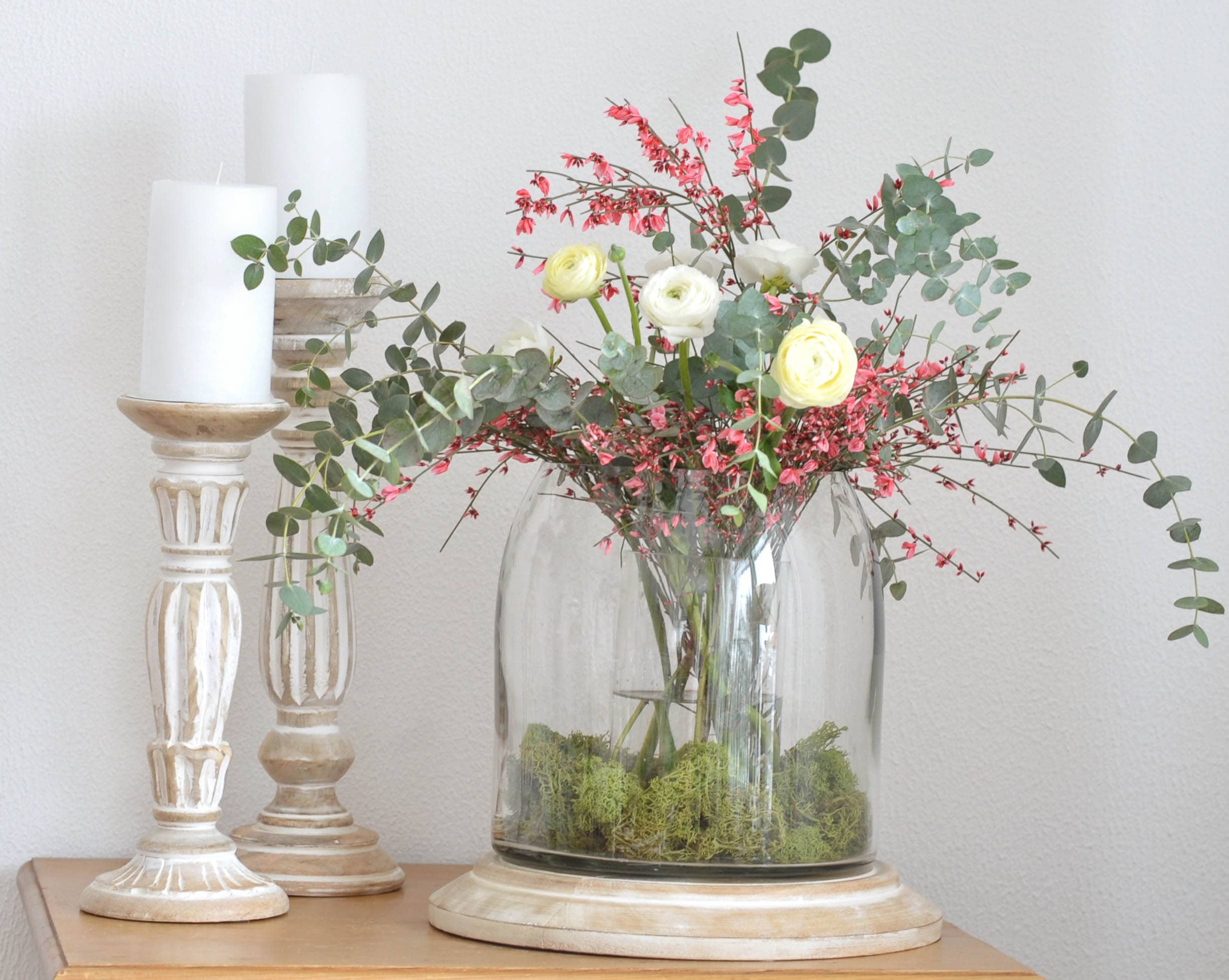 Decoratief boeket met witte en roze bloemen in glazen vaas op houten voet met witte kaarsen
