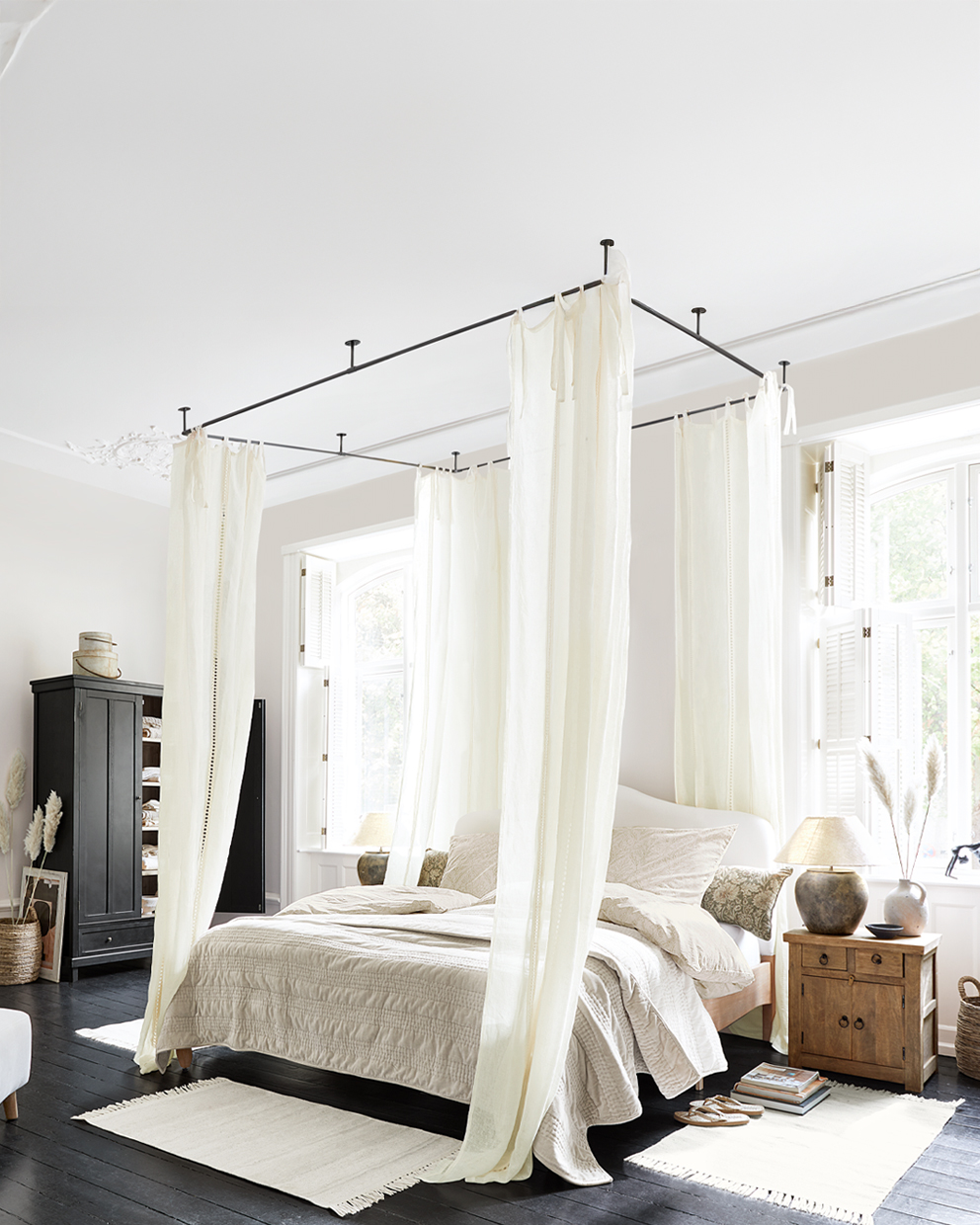 Slaapkamer met hemelbed en crèmekleurige gordijnen, houten nachtkastje en lichte accessoires