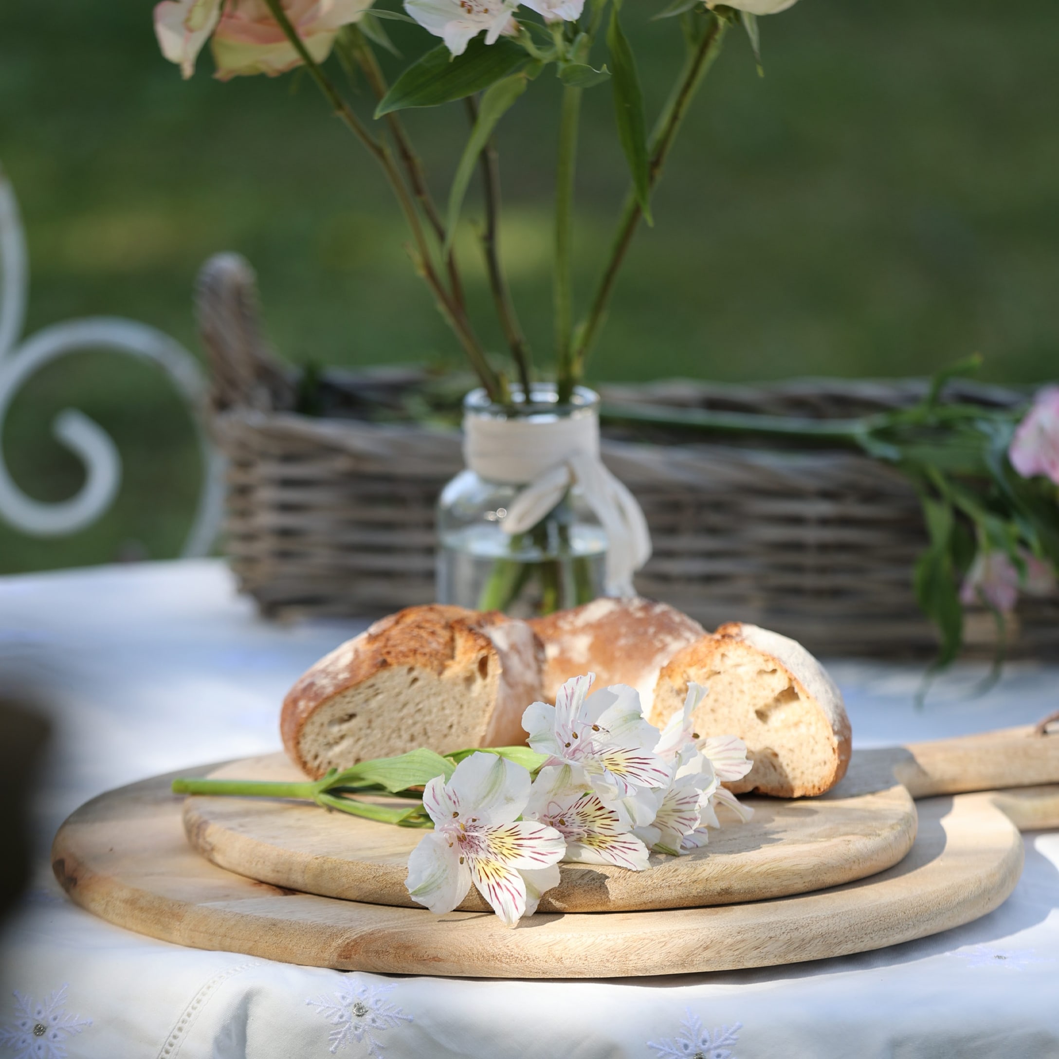 Houten snijplank met witte bloemen en broodstukken op een buitentafel in de tuin