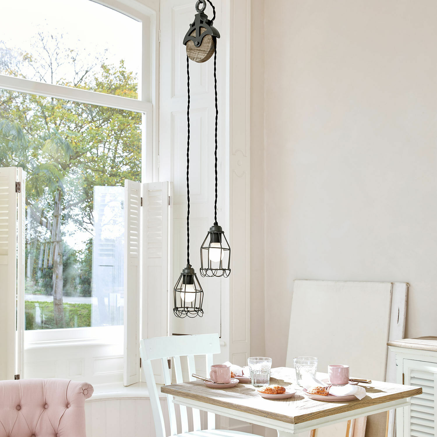 Twee zwarte metalen hanglampen met beschermkooi boven houten tafel in lichte kamer