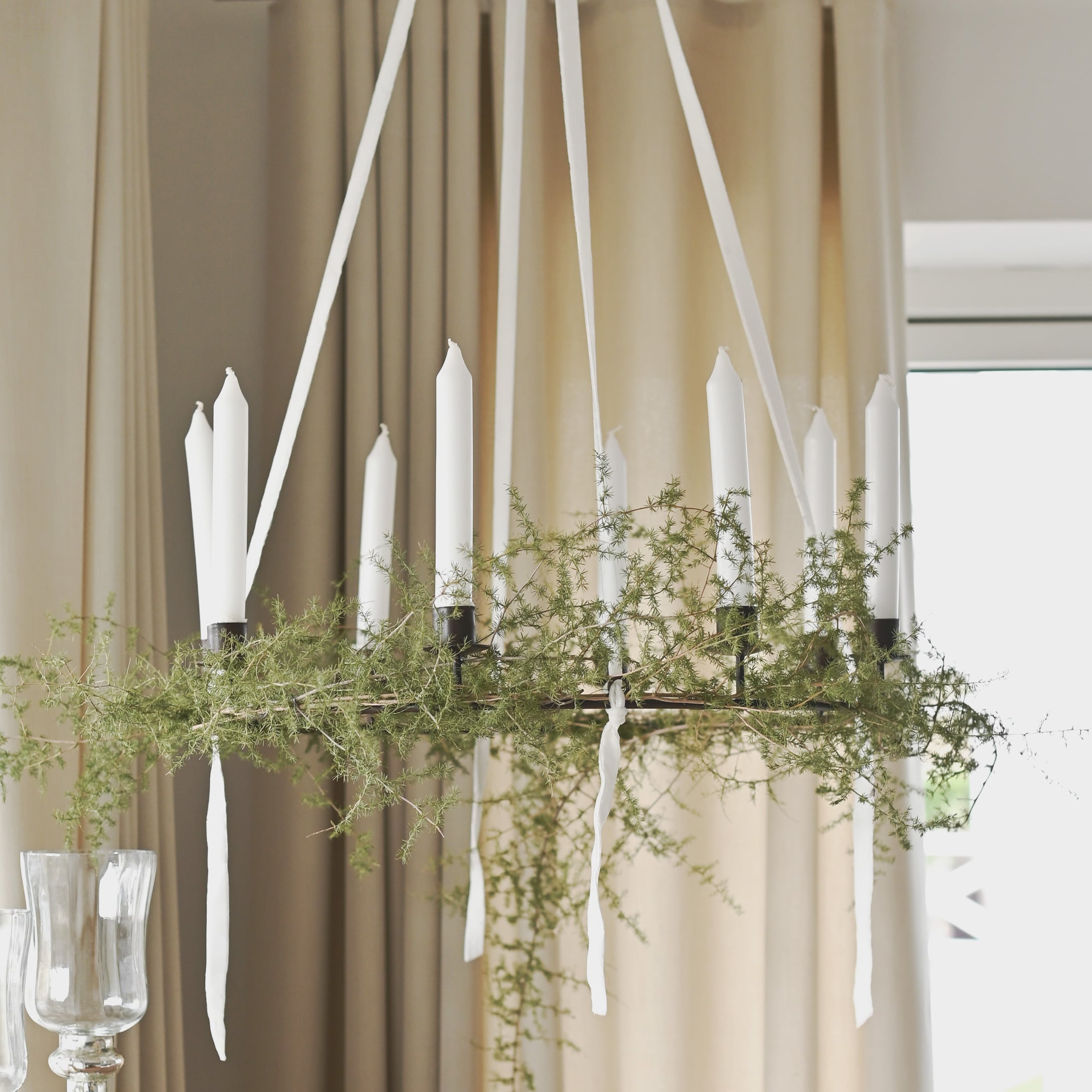 Decoratieve krans met witte kaarsen en groene takken hangend in lichte woonkamer