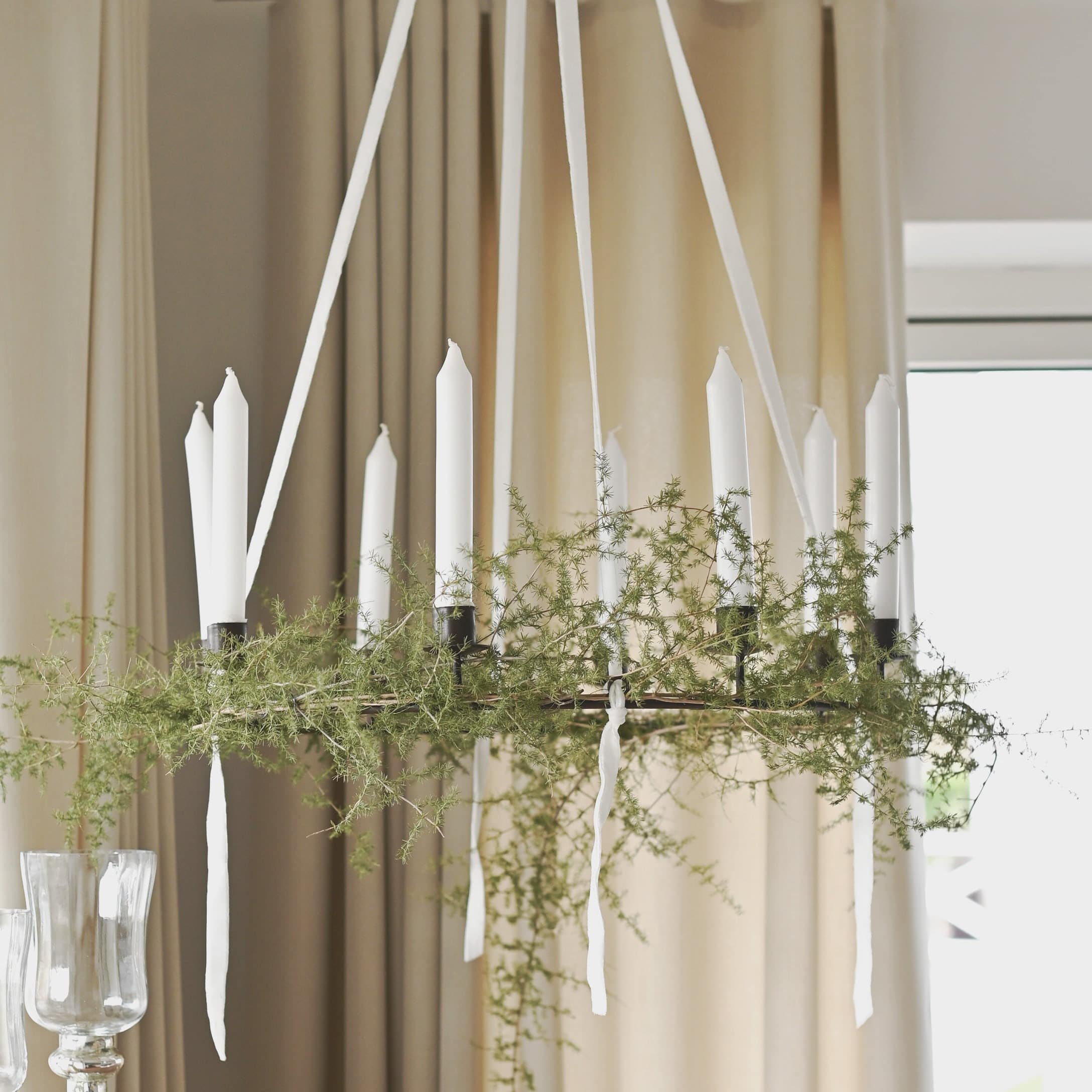 Decoratieve krans met witte kaarsen en groene takken hangend in lichte woonkamer