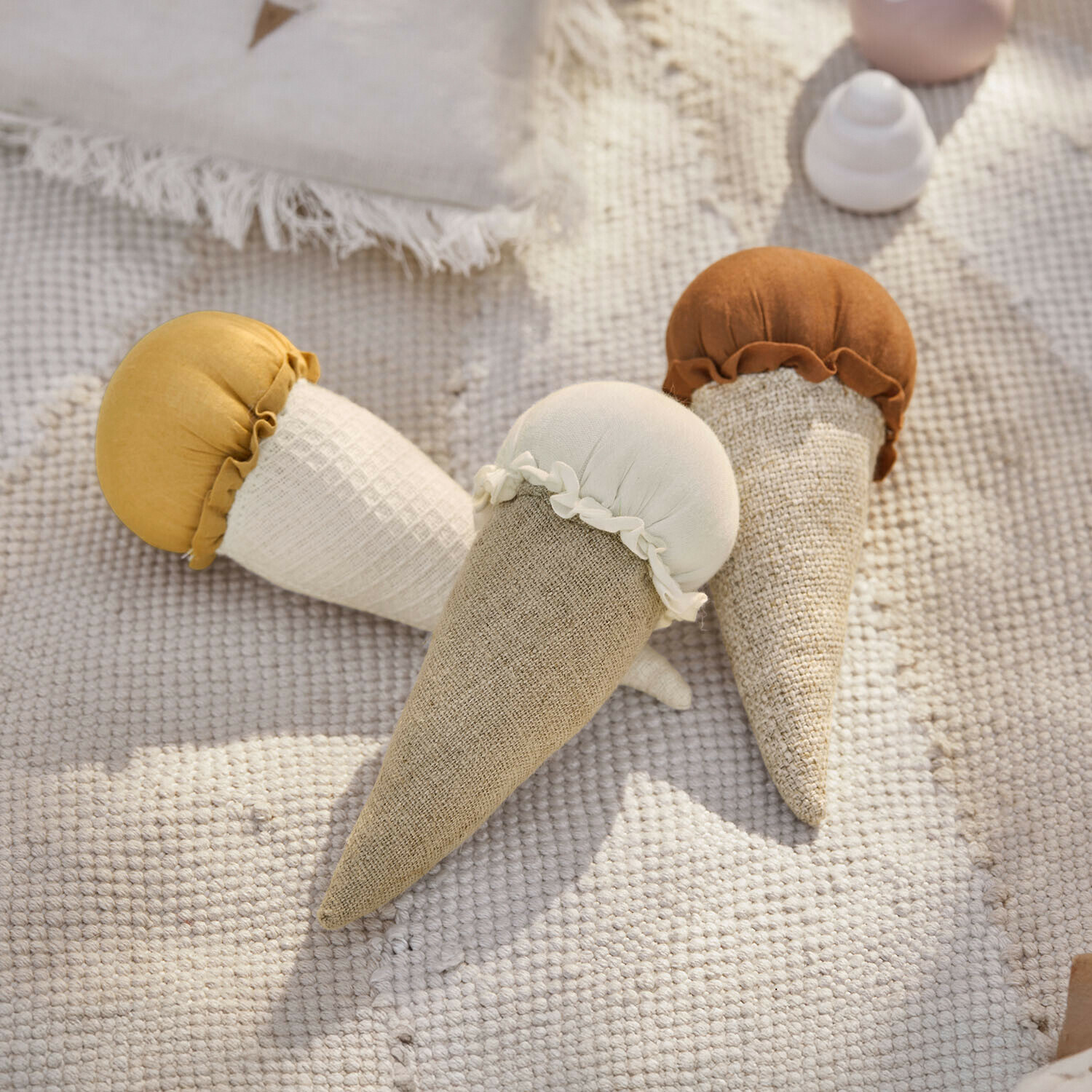 Drie zachte stoffen ijsvormige speelgoedjes in beige, wit en bruin op een lichte vloerbedekking