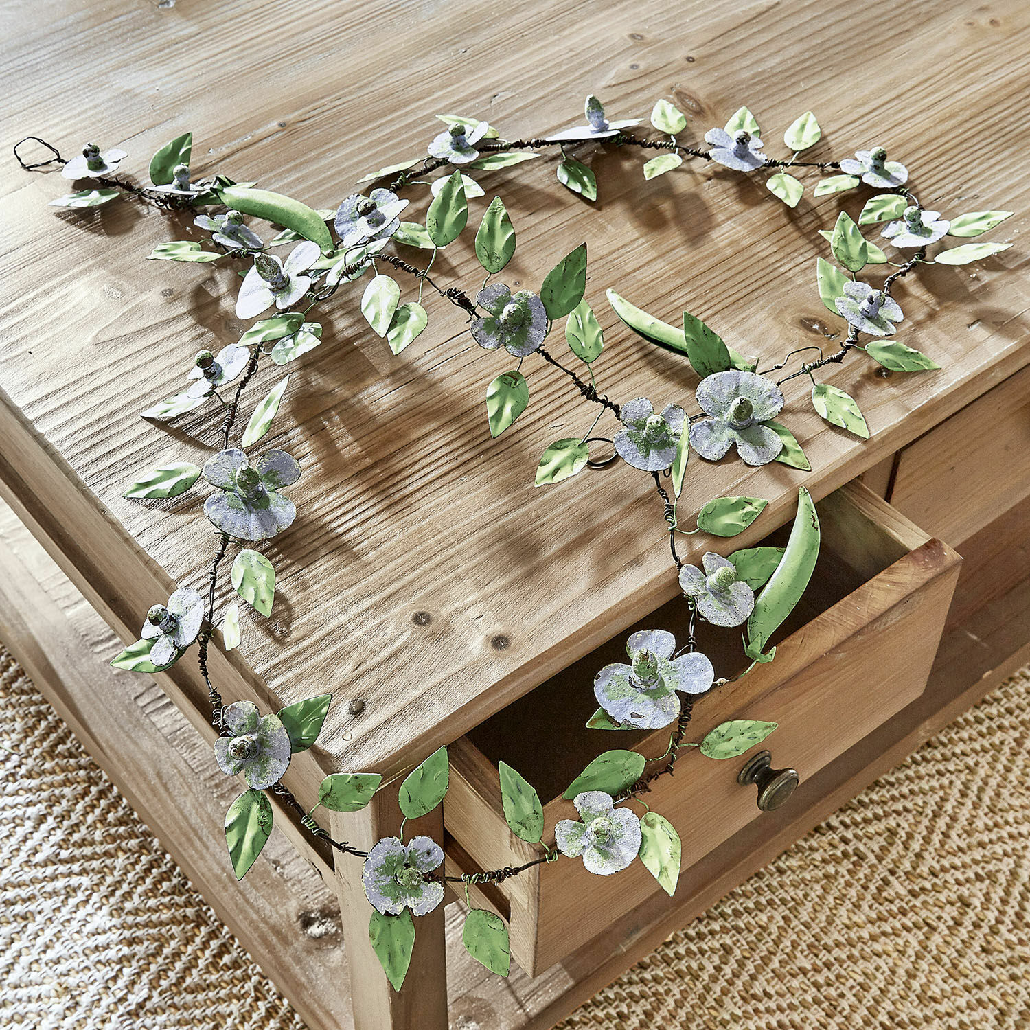 Guirlande Cecilia Decoratieve metalen krans met groene en grijze bloemen en bladeren op een lichte houten tafel