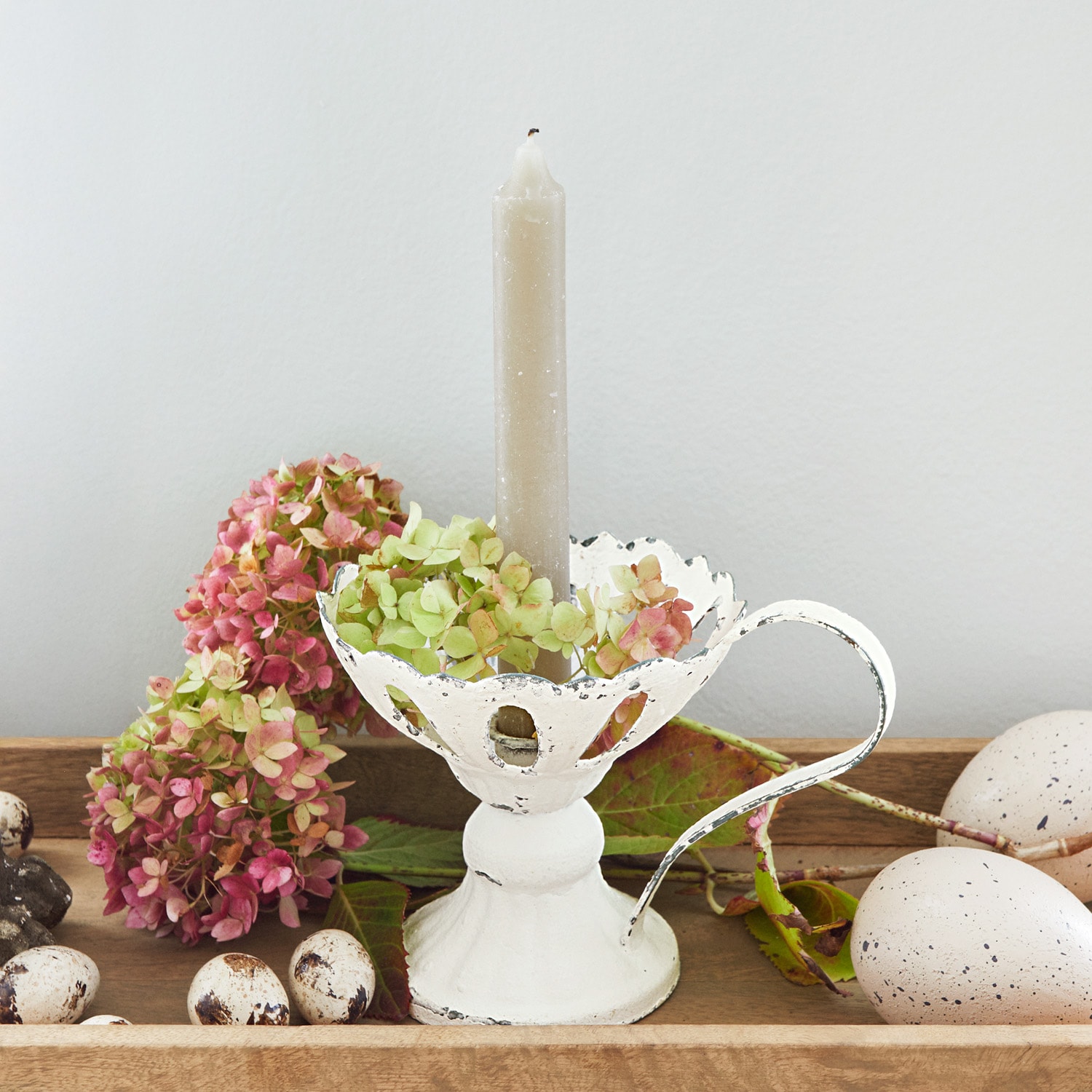 Witte metalen kandelaar met handvat en grijze kaars, versierd met bloemen en decoratieve eieren