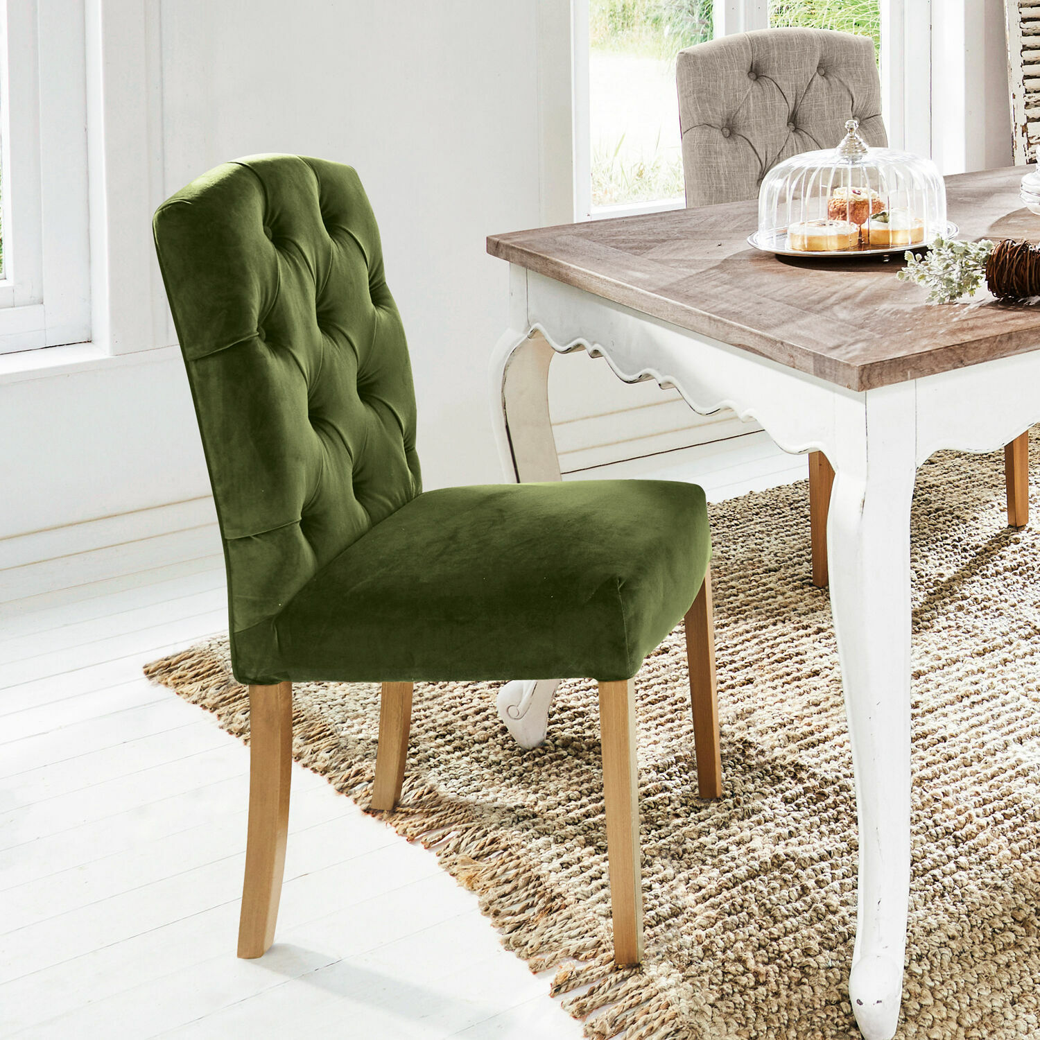 Groene fluwelen stoel met houten poten bij witte tafel in lichte kamer