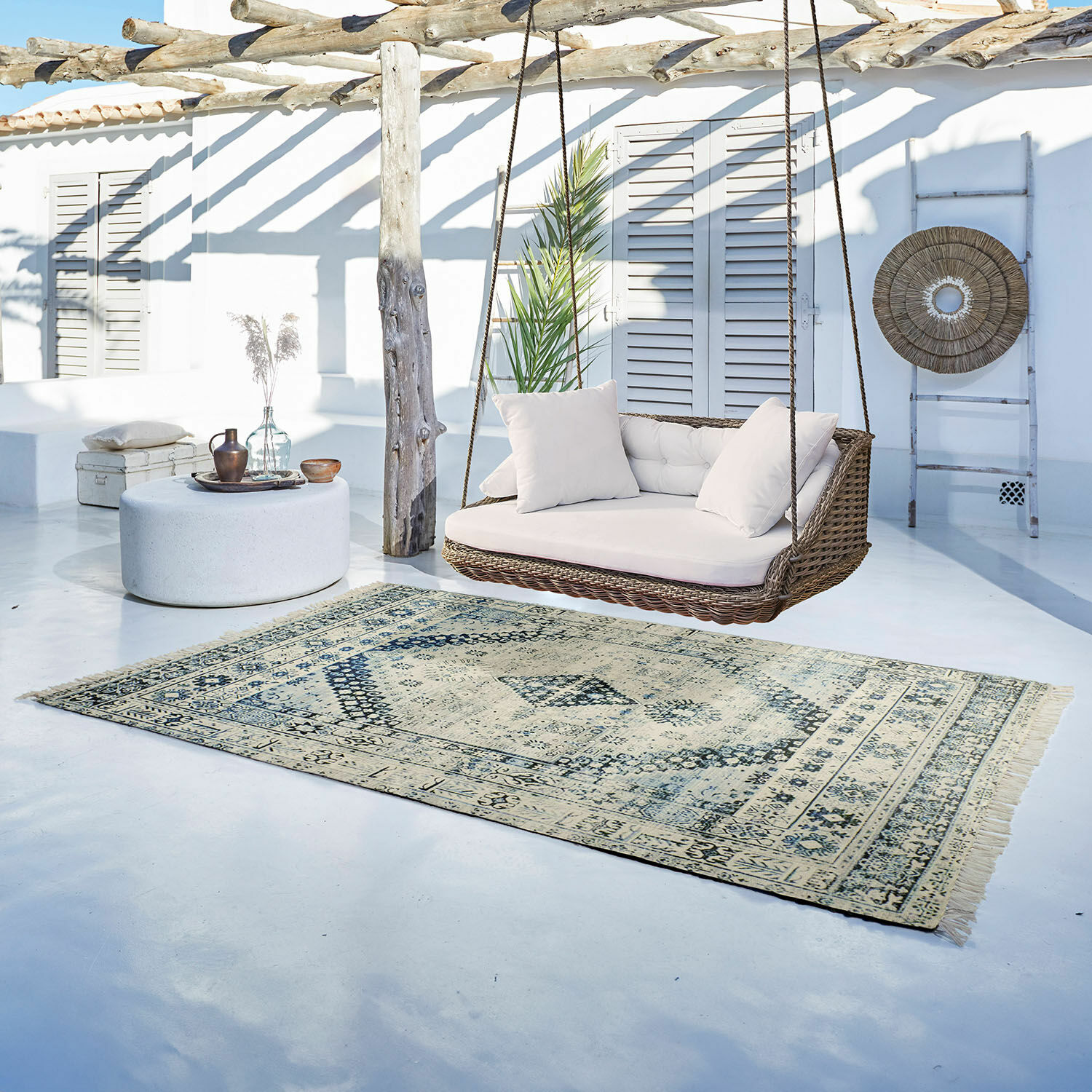 Vloerkleed voor binnen en buiten Daly Vintage vloerkleed in beige en lichtblauw op lichte vloer naast rotan schommel met witte kussens