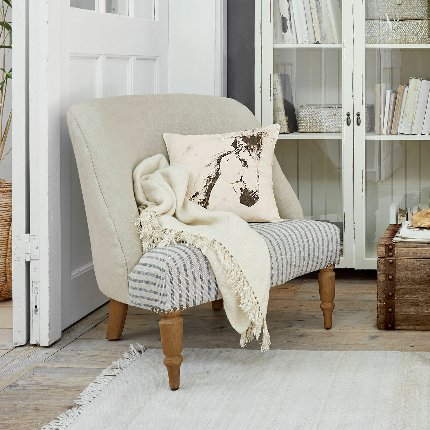 Tweekleurige bank met beige rugleuning en gestreept zitvlak, paardenkussen en crème deken