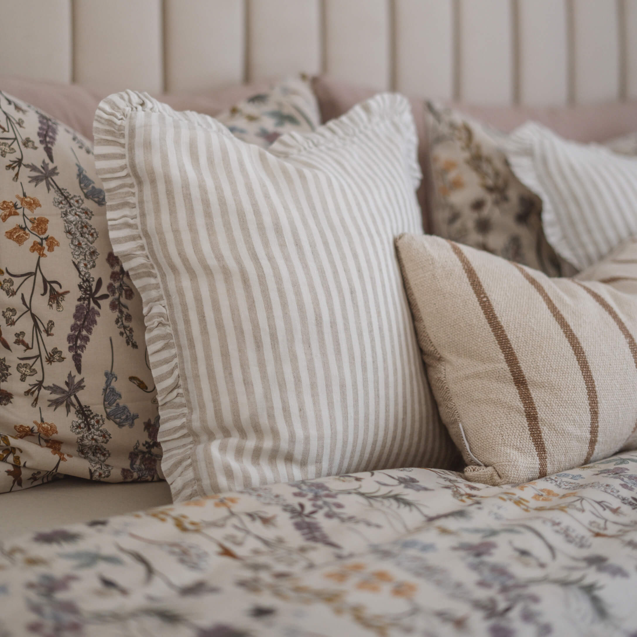 Set decoratieve kussens met beige strepen en bloemenpatroon op bed in slaapkamer