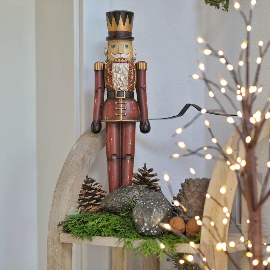 Rode houten notenkraker met zwarte hoed op decoratieve plank met groene takken en dennenappels