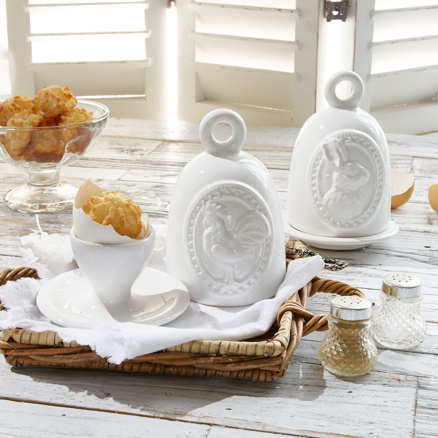 Witte keramische potten met haan- en konijnmotief op rustieke houten tafel met snacks
