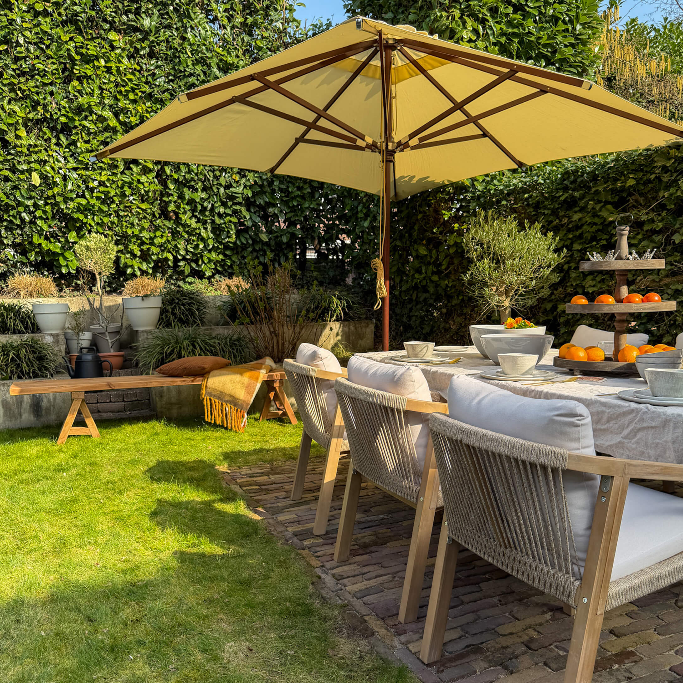 Tuinmeubelset met houten stoelen en gele parasol op groen gras in zonnige tuin