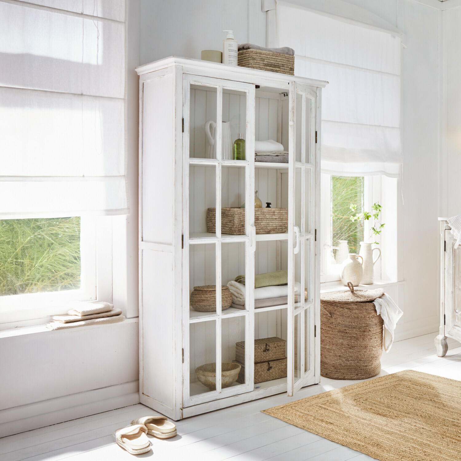 Witte houten kast met glazen deuren in lichte kamer met natuurlijke decoraties en textiel