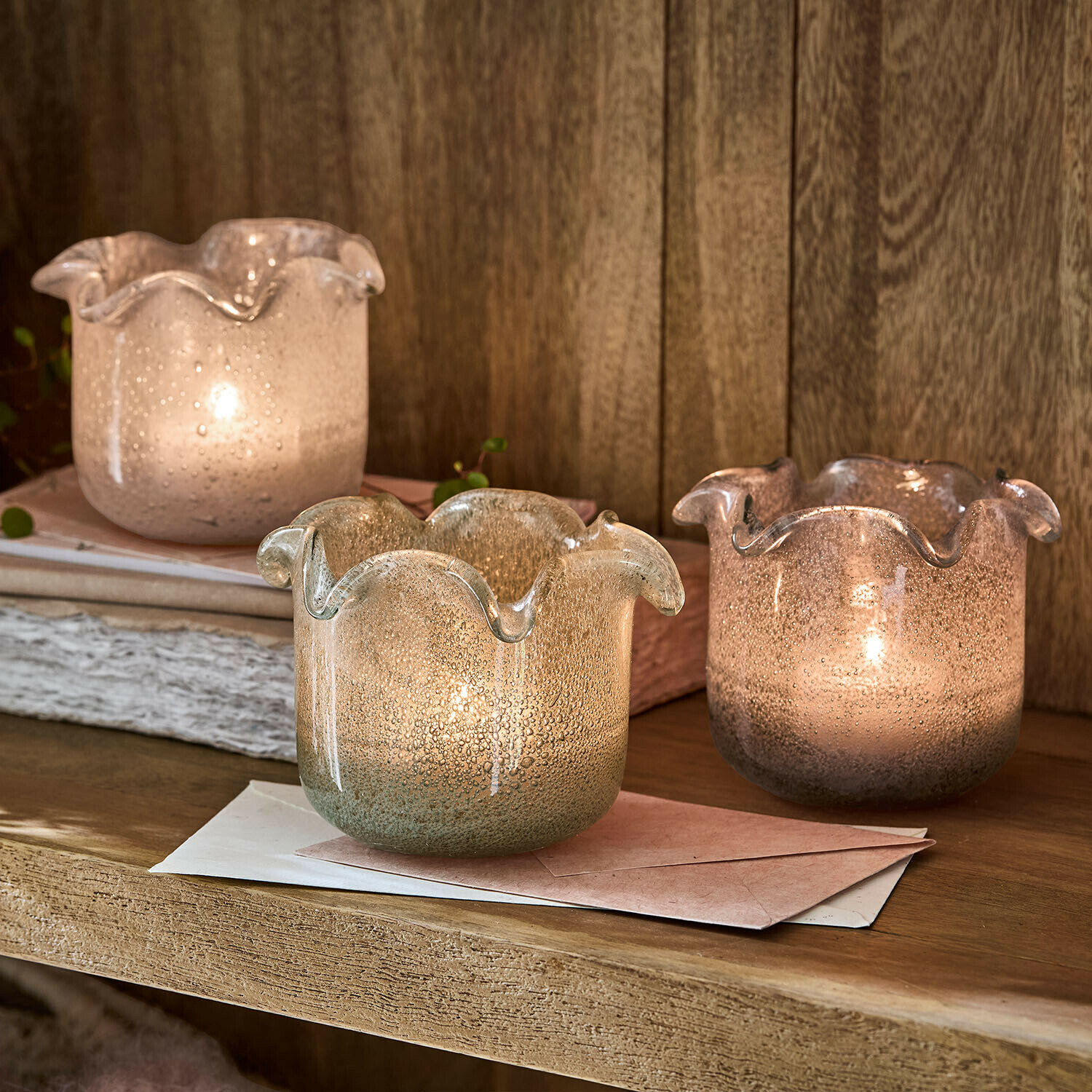 Drie decoratieve theelichthouders van geblazen glas in pasteltinten op een houten plank