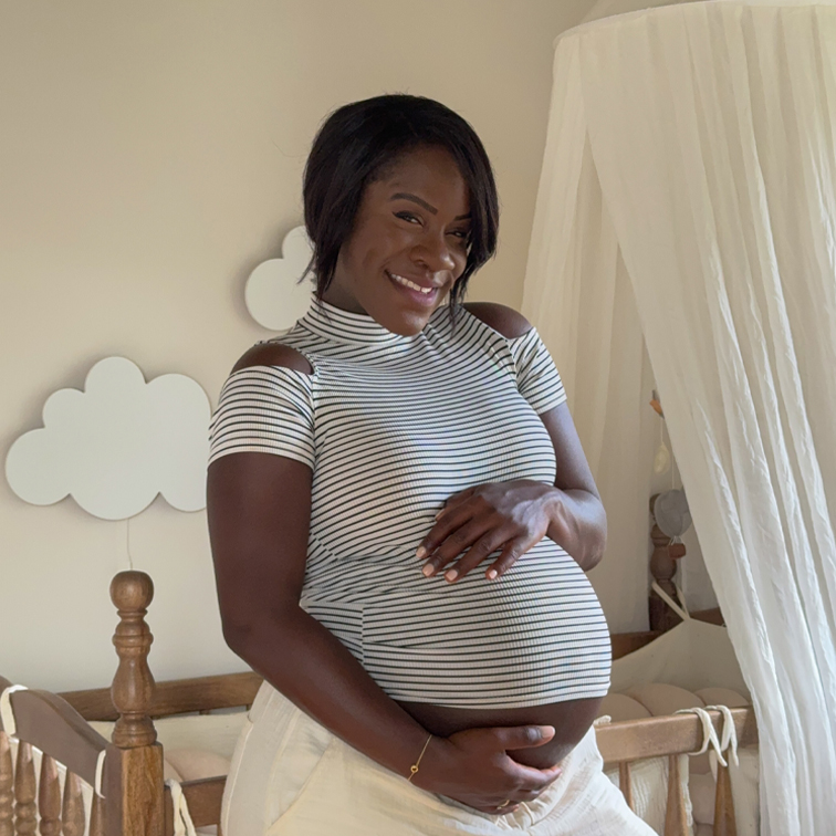 Lachende zwangere vrouw in gestreept shirt in lichte kamer met houten babybedje
