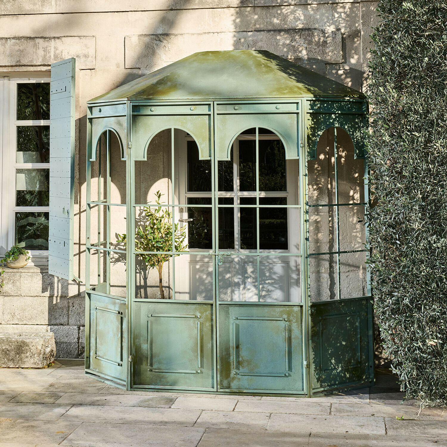 Groene metalen tuinpaviljoen met glazen panelen en dak, perfect voor buitenruimte