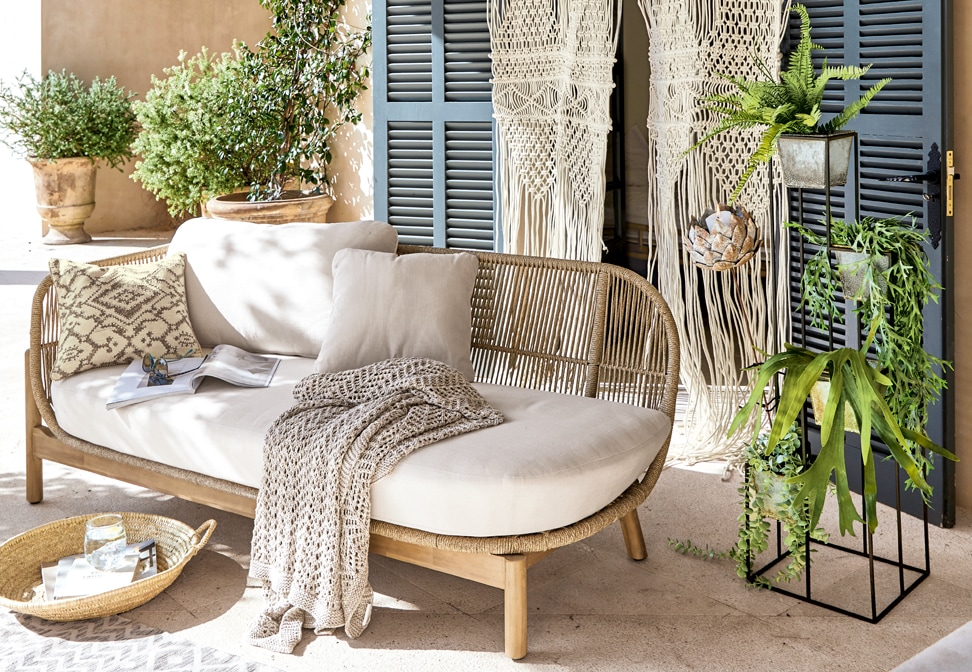 Boho bank met lichtbeige bekleding en houten frame, versierd met kussens en een gebreide deken