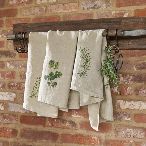 Linnen keukendoeken in natuurlijke kleur met kruidenprint aan houten rek voor een bakstenen muur