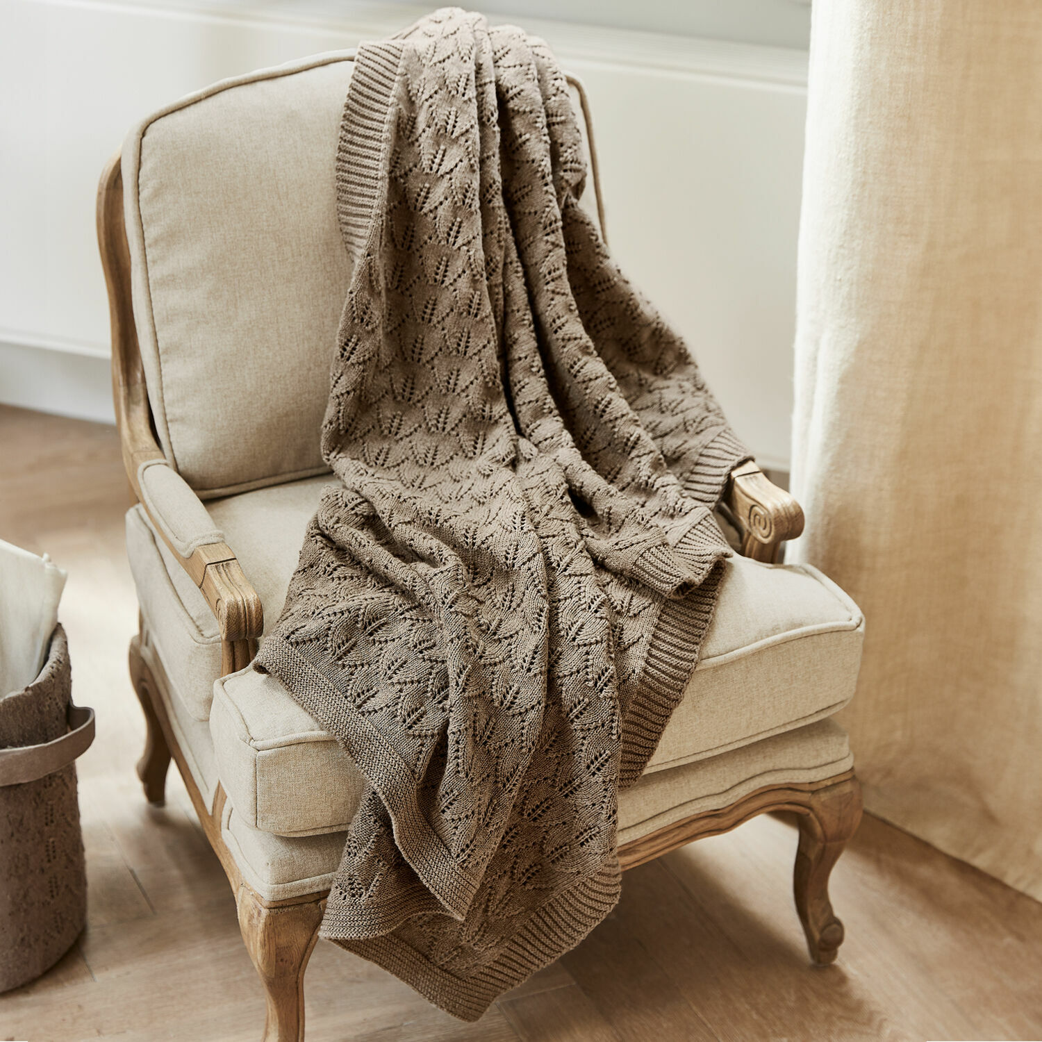 Babydekentje Ernival Beige gebreide katoenen deken op crèmekleurige stoel met houten poten in lichte kamer