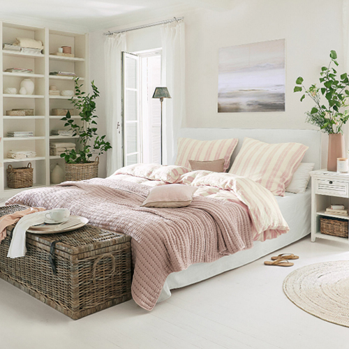 Gezellige slaapkamer met wit beddengoed en roze deken, natuurlijke decoraties en rieten kist