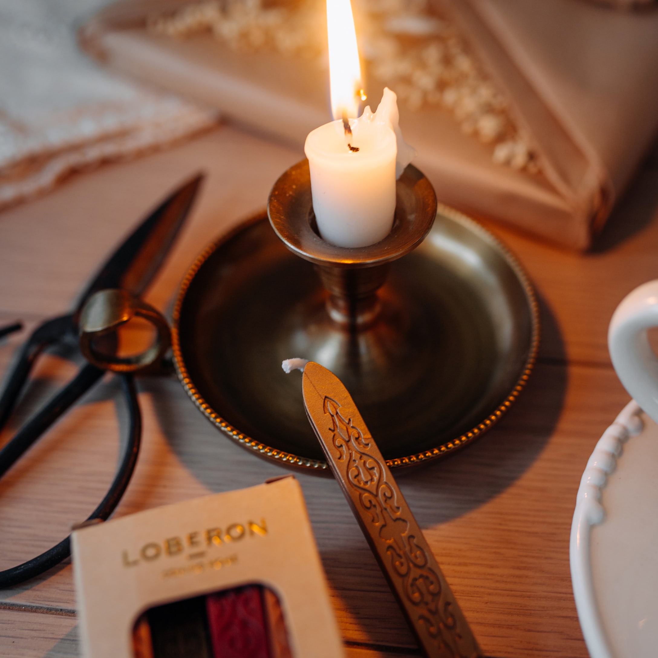 Witte kaars in messing kandelaar met cadeauverpakkingsgereedschap op houten tafel