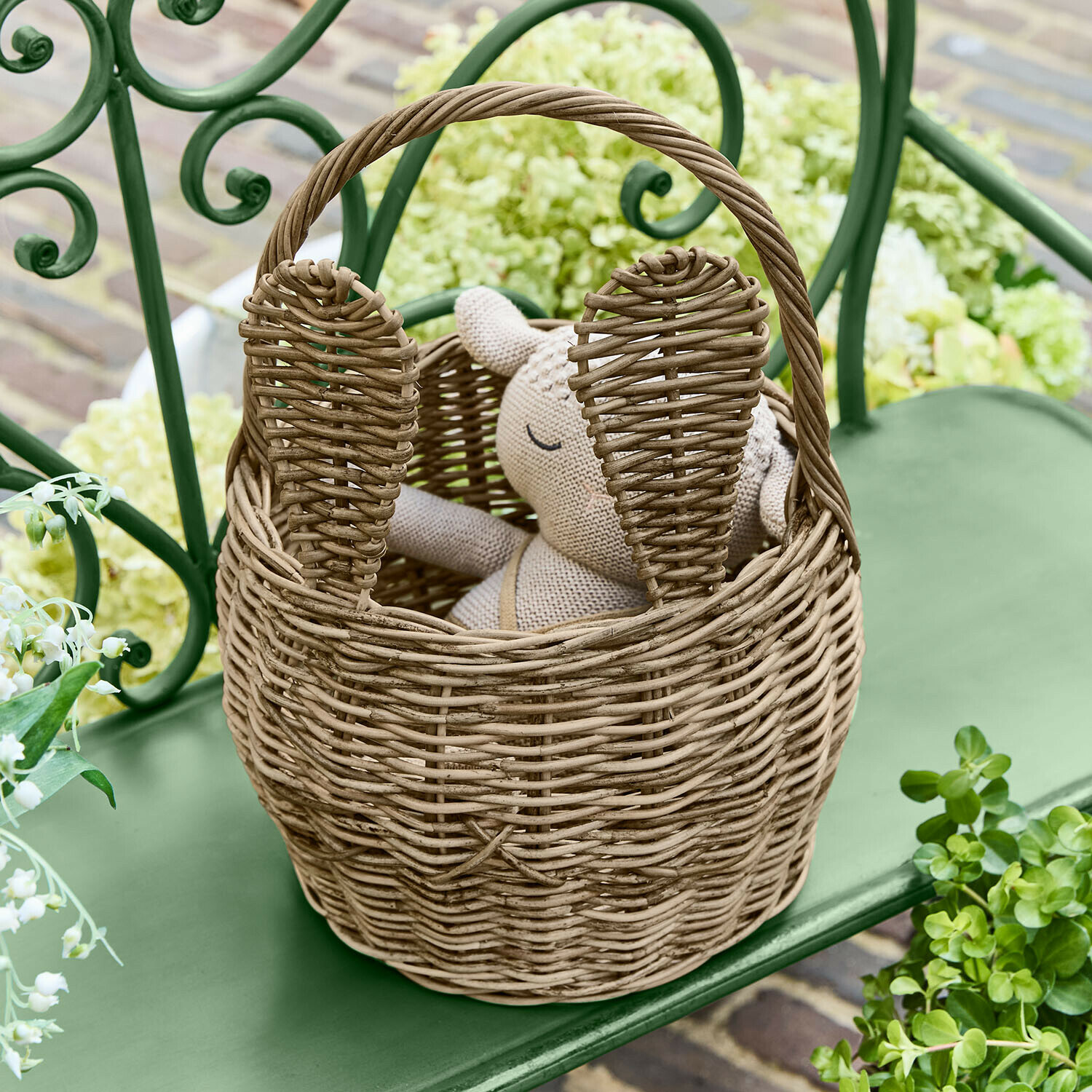 Natuurlijke rieten mand in konijnenvorm met oren, op een groene tuinbank geplaatst