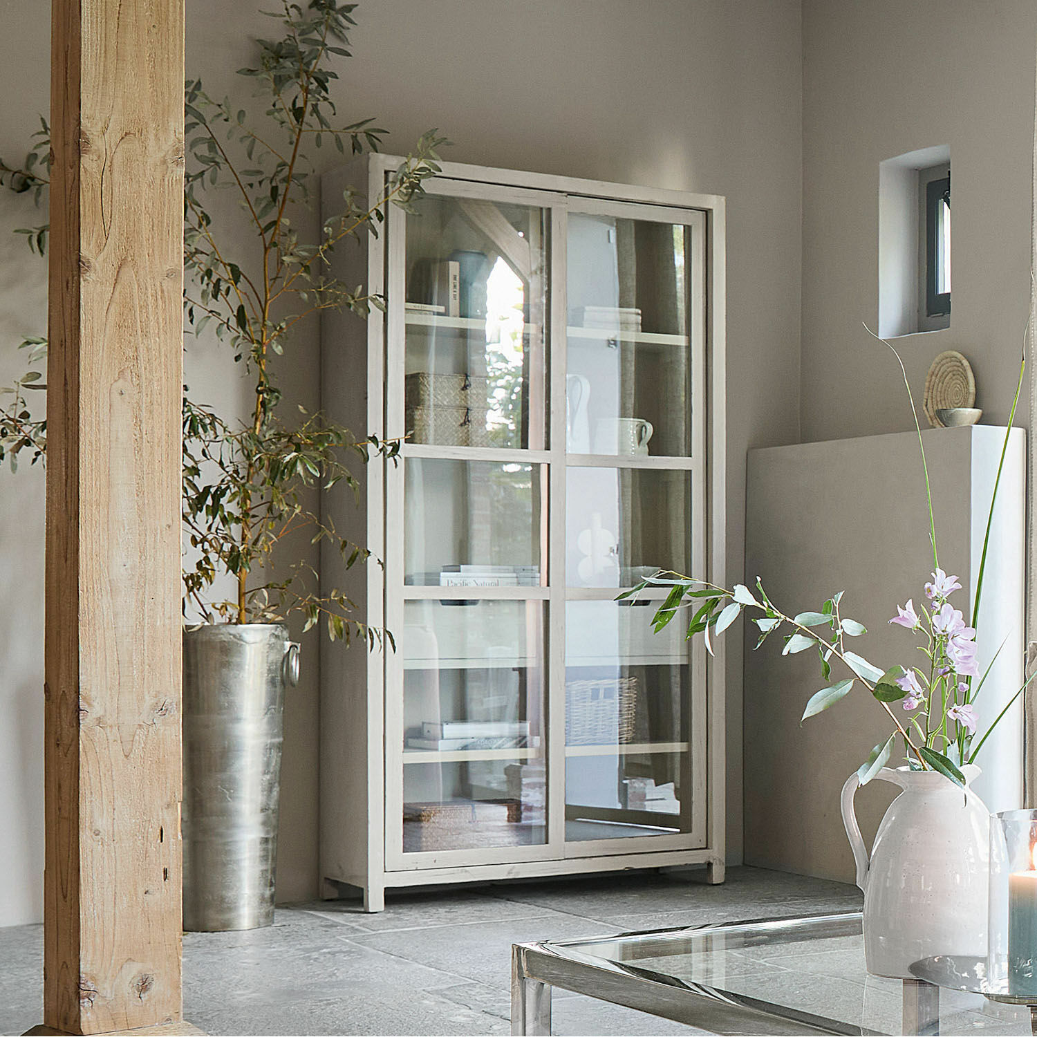 Witte houten vitrinekast met glazen deuren in moderne woonkamer met planten en decoratie