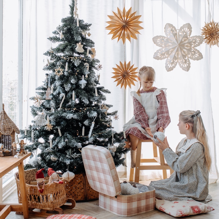 Kinderen bij een versierde kerstboom met natuurlijke ornamenten en papieren sterren in een lichte kamer