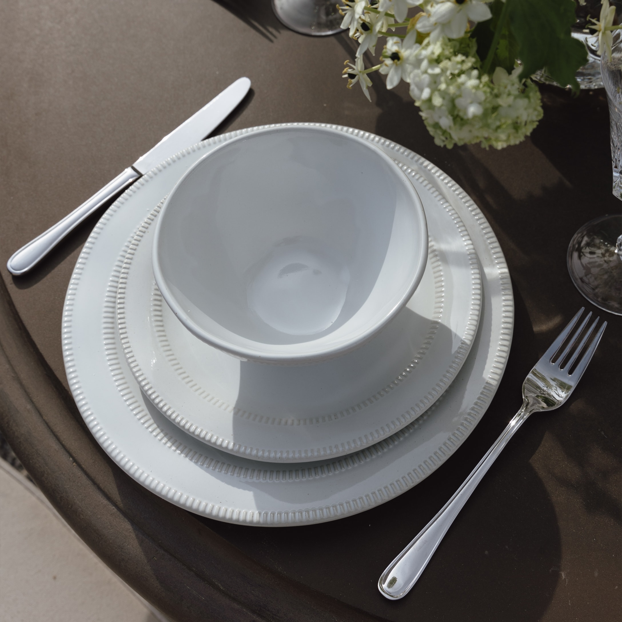 Wit porseleinen servies met kom en borden op bruine tafel met bloemen en bestek