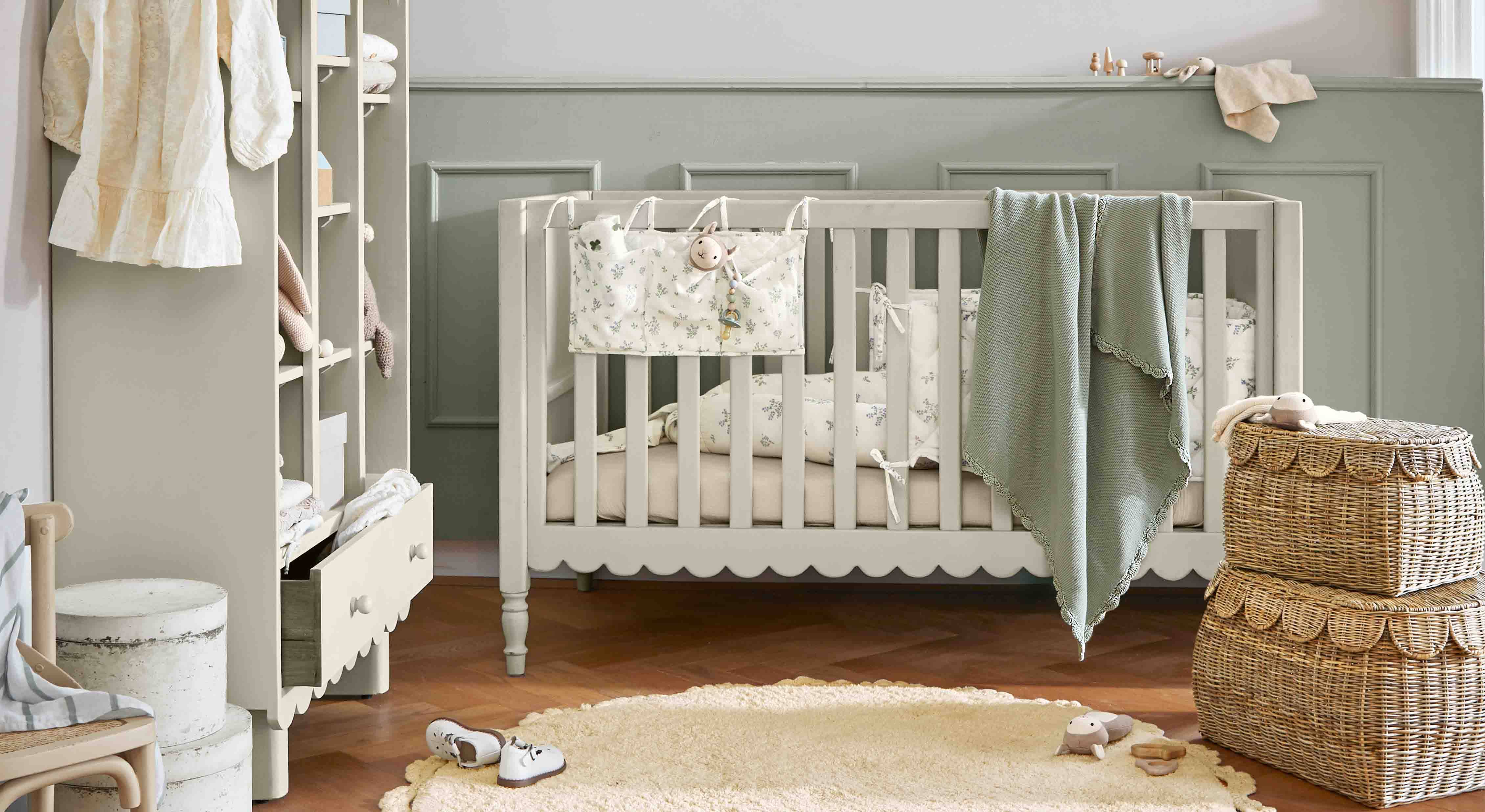 Grijs houten babybed met groene deken en rieten manden in een gezellige kinderkamer