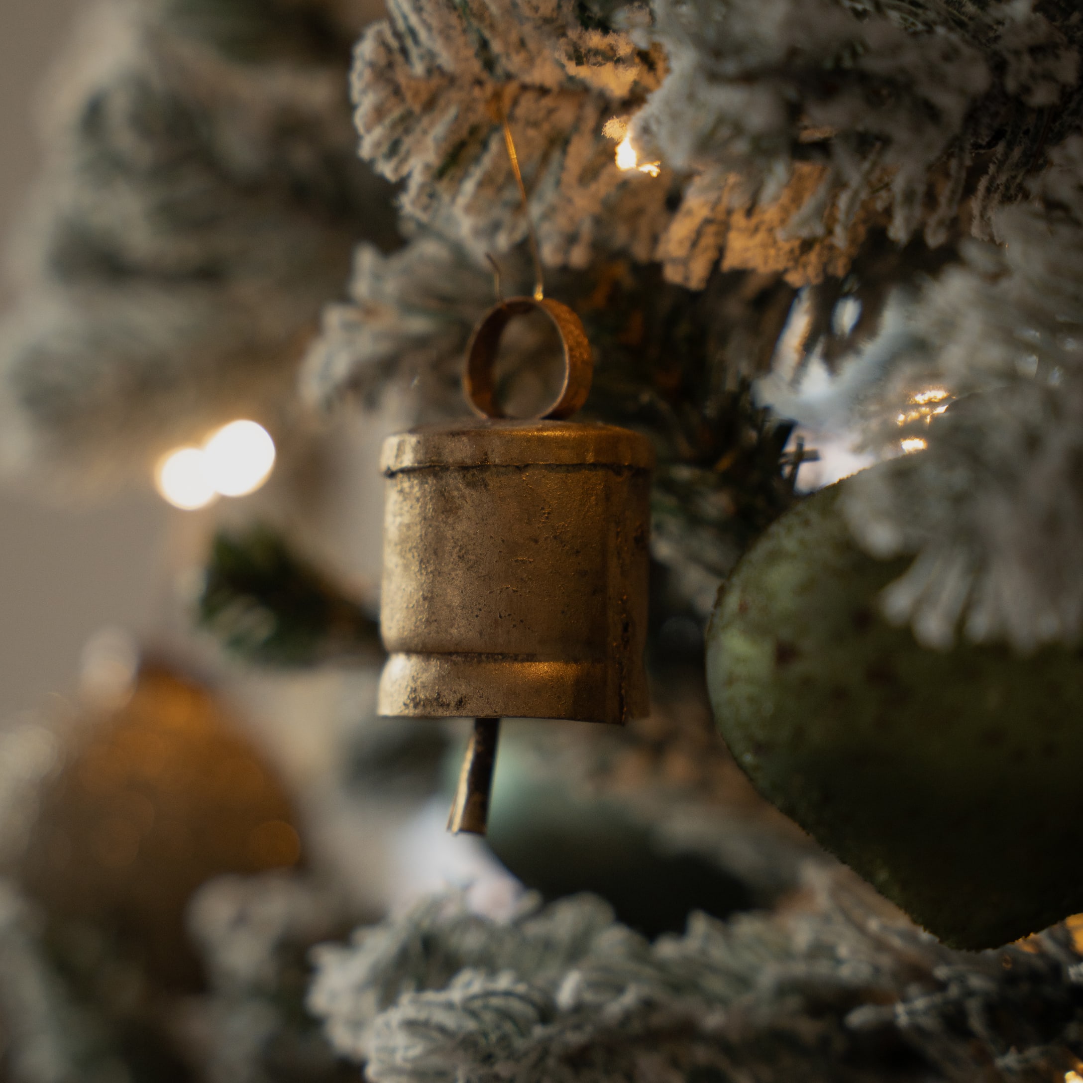 Gouden metalen bel aan besneeuwde kerstboom met feestelijke verlichting en decoraties