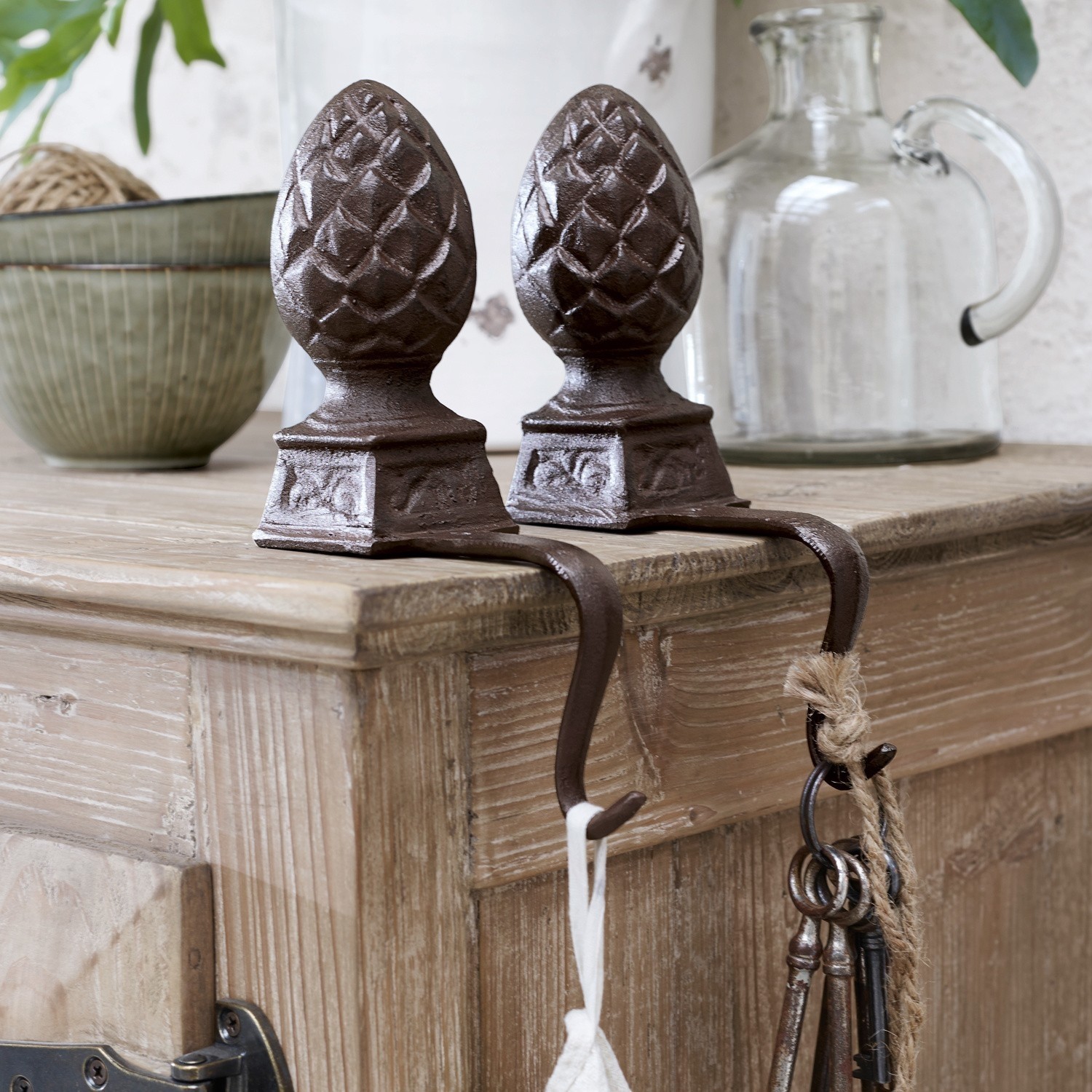 IJzeren dennenappel set van 2 Lucielle Set van twee bruine decoratieve gietijzeren haken in dennenappelvorm op een lichte houten tafel