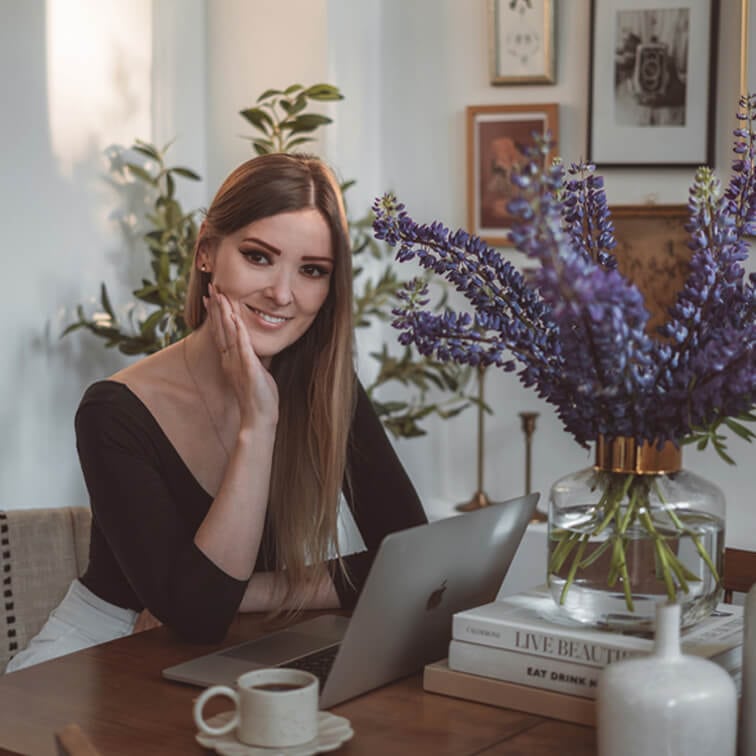 Vrouw die aan een houten tafel met laptop werkt, paars boeket bloemen en koffiekopje