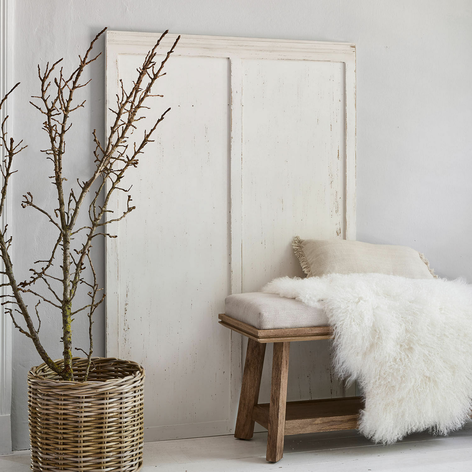 Houten bankje met beige kussen en witte bontdeken naast een rieten mand met takken