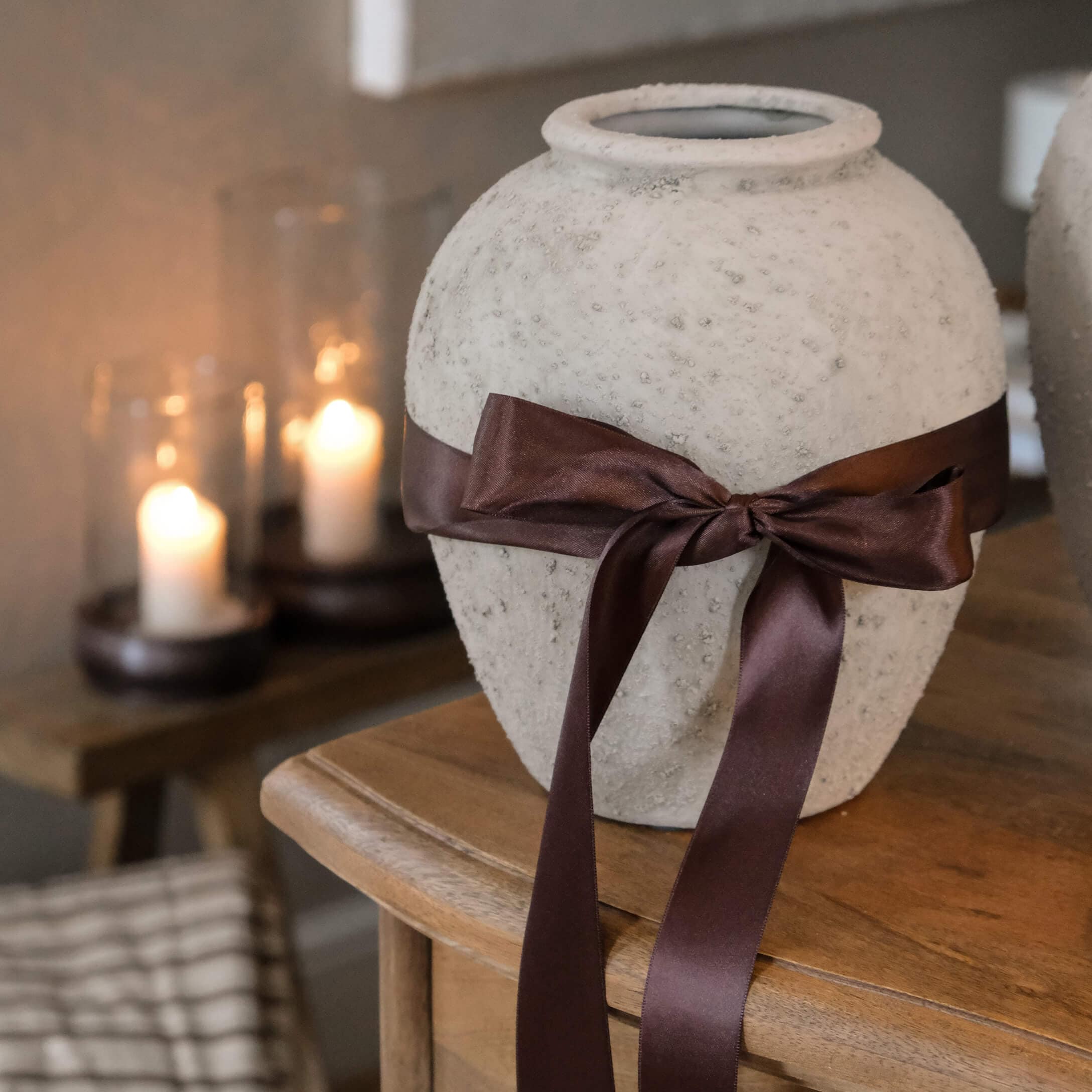 Decoratieve witte vaas met structuur en bruine satijnen strik op houten tafel in gezellige ruimte