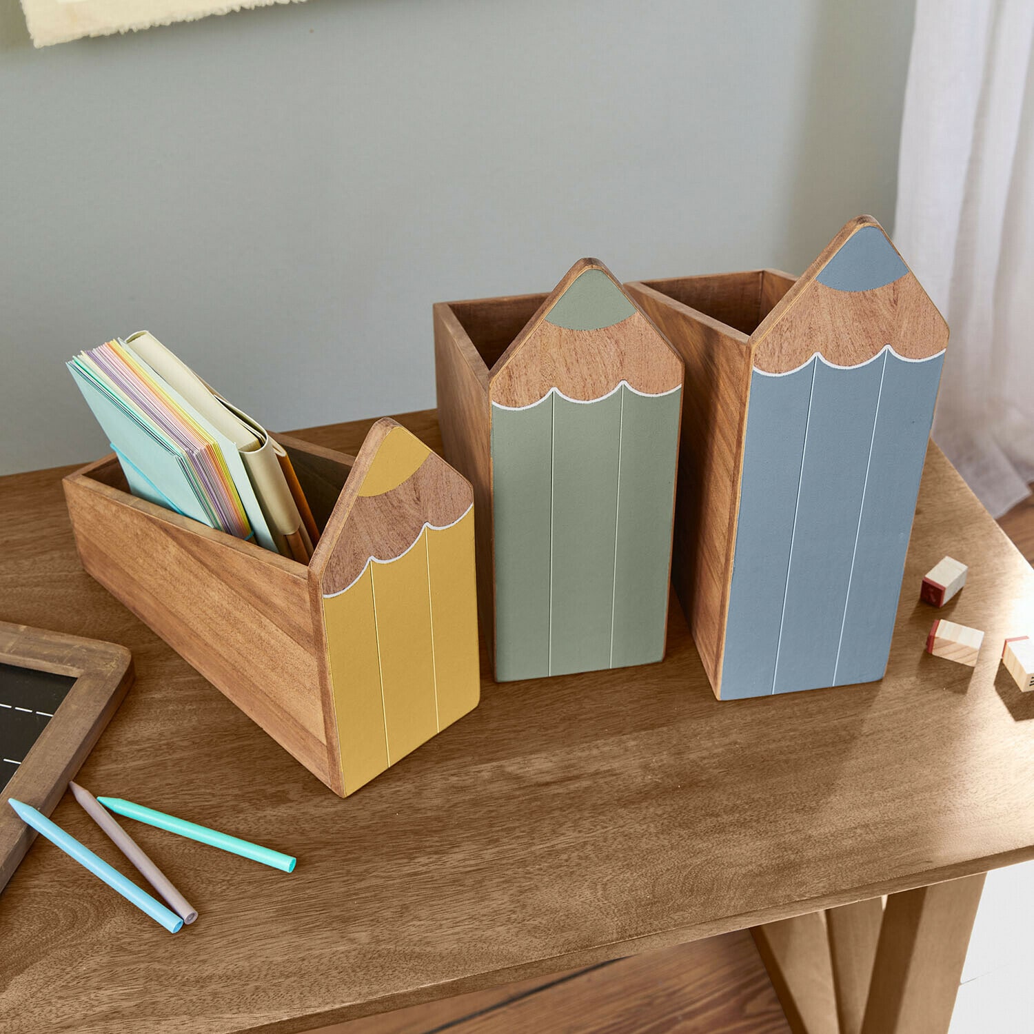 Set van drie houten potloodvormige organizers in geel, groen en blauw op een houten bureau